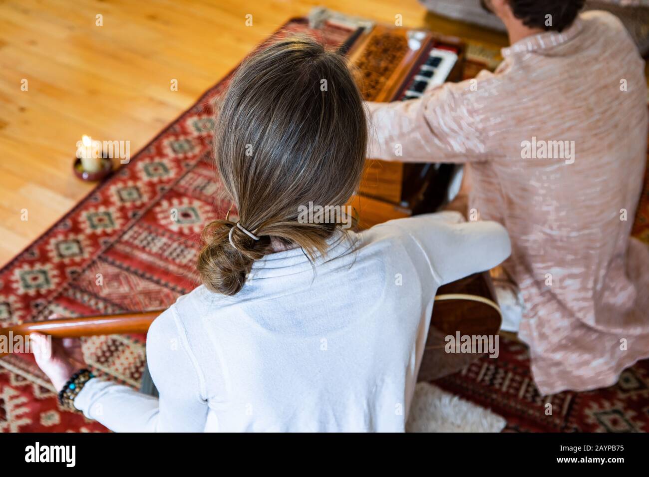 Vue en grand angle des femmes et des hommes jouant de la musique apaisante à l'aide de la guitare classique et de l'harmonium. Avec la bougie brûlant et assis sur le tapis de sol dans la chambre Banque D'Images