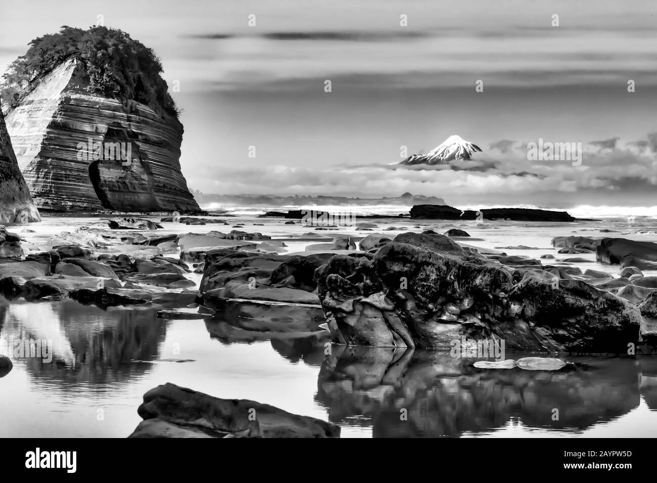 De belles formations rocheuses à la plage avec le cône volcanique du Mont Egmont au loin Banque D'Images