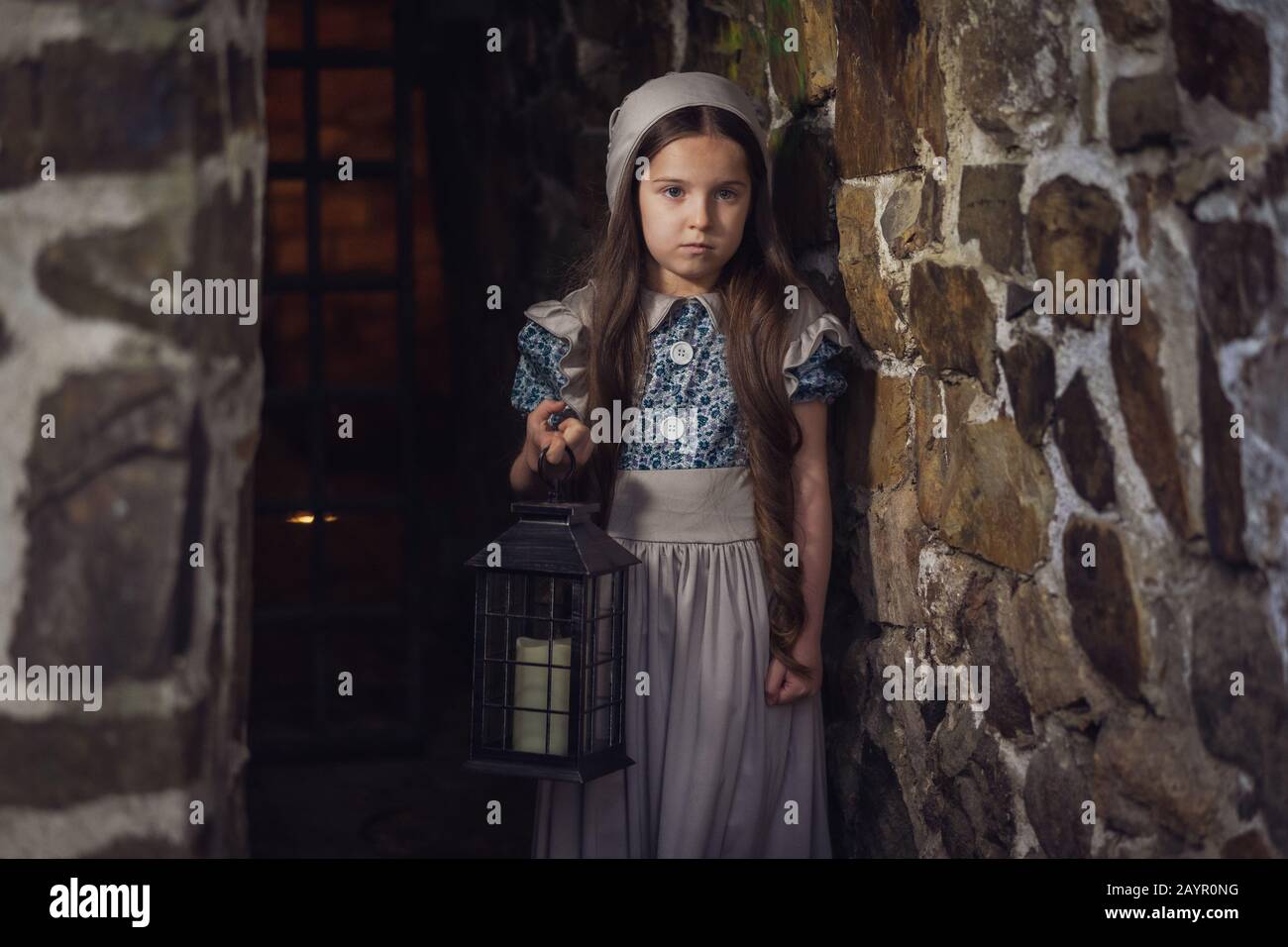 Fille effrayée dans les donjons d'un château ancien. Dans sa lanterne à main. Stylisation. Tonification vintage. Banque D'Images