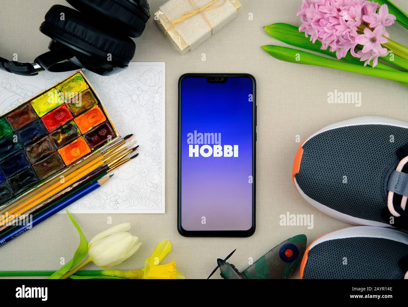 Logo de l'application HOBBI sur le smartphone et pièces représentant les hobbies populaires. Facebook a récemment publié l'application appelée Hobbi. Photo à plat. Banque D'Images