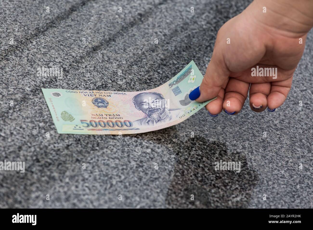 Une femme main gauche, des ongles bleus. Ramasse le billet d'argent vietnamien de 50000 dong sur le sol Banque D'Images