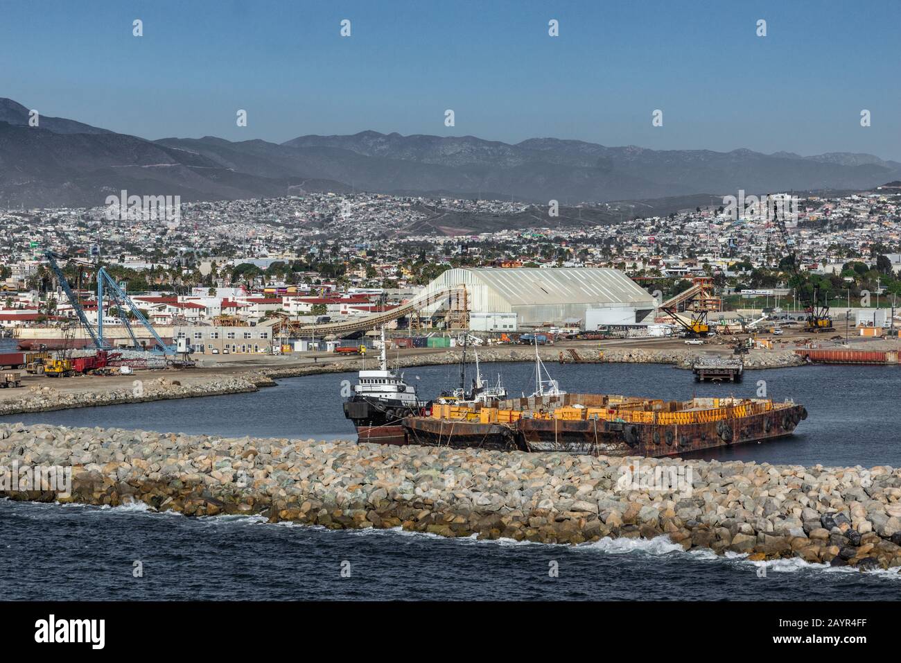 Ensenada, Mexique - 17 janvier 2012: Grand bâtiment blanc exploitant le déchargement en vrac et la charge de minéraux par le biais de la ceinture de transport sur les navires. Barges devant le tourbillon Banque D'Images