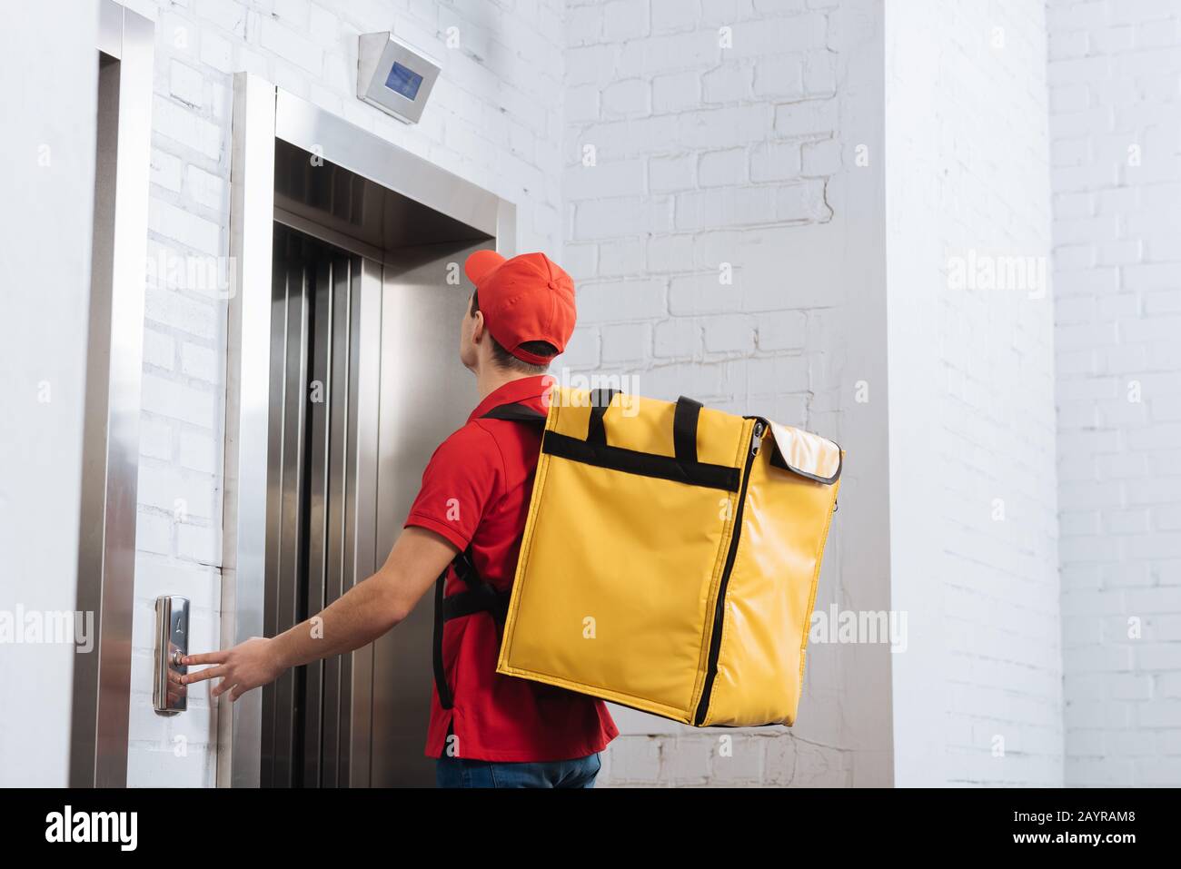 Vue latérale de l'homme de livraison avec bouton d'ascenseur à enfoncer thermo sac à dos Banque D'Images