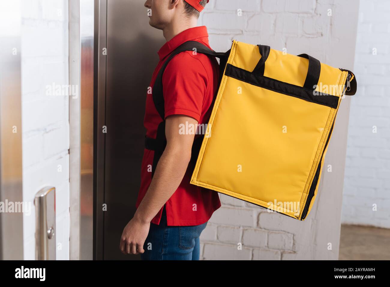 Vue réduite de l'homme de livraison avec sac à dos thermo debout près de l'ascenseur Banque D'Images