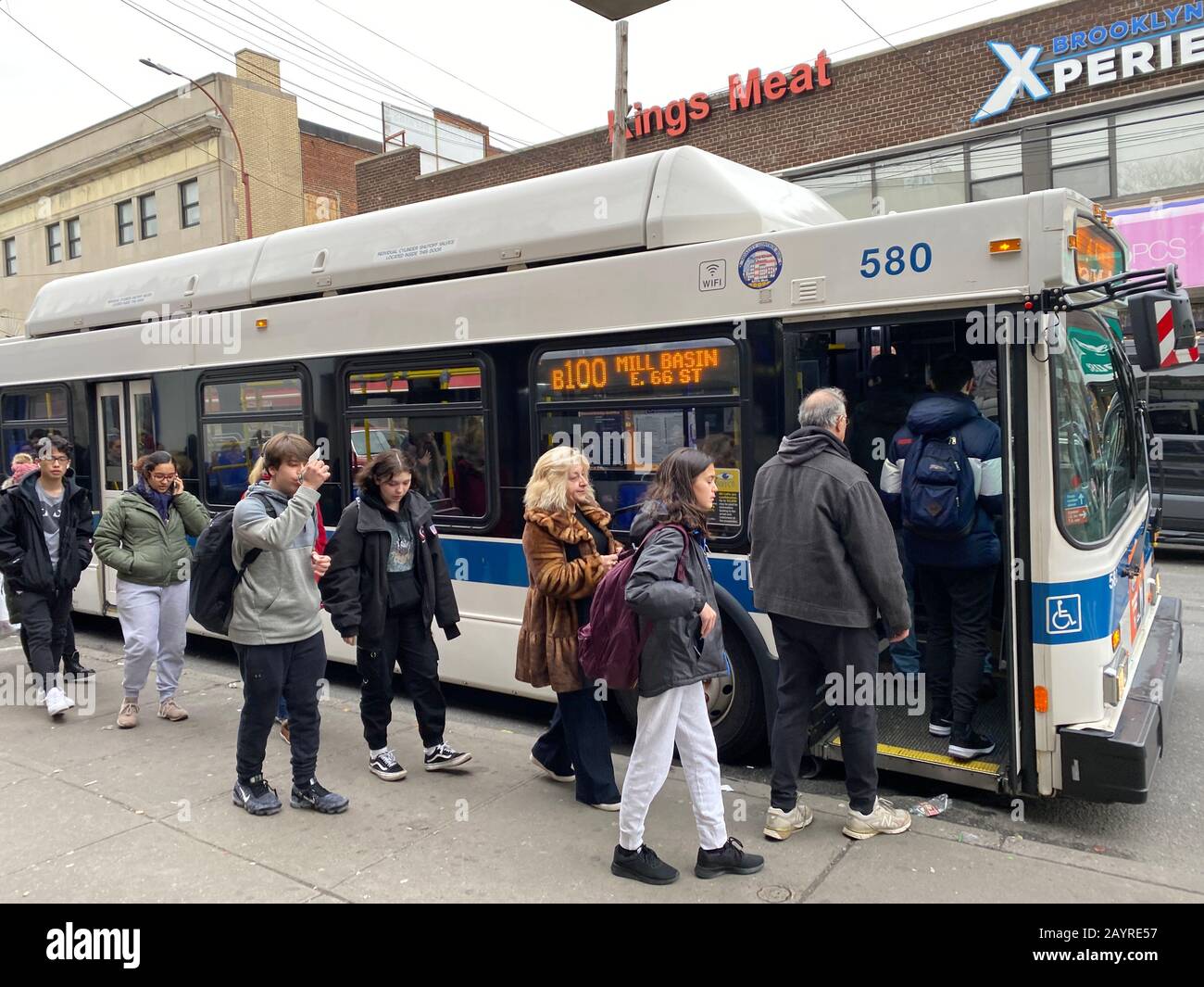 File d'attente des lycéens et d'autres attendent pour prendre un bus NYC sur Quentin Road dans le quartier Midwood de Brooklyn, New York. Banque D'Images