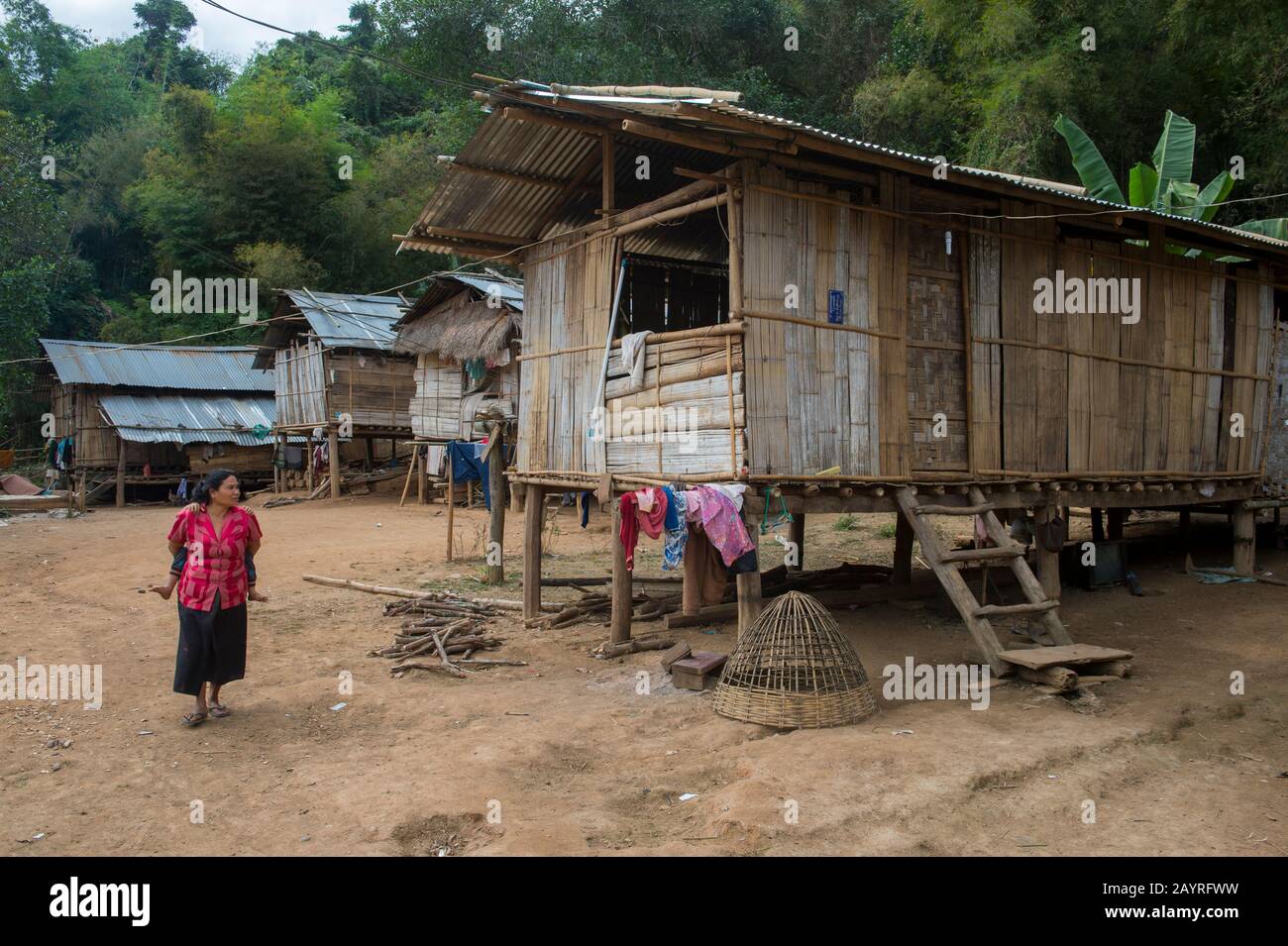 Une femme locale marche devant des maisons traditionnelles sur pilotis en bambou dans le village Ban Muangkeo, un village du patrimoine culturel du Mékong Banque D'Images