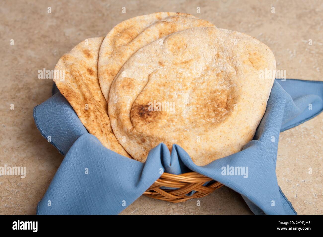 Trois pains ronds de pita dans un panier en osier avec une serviette en tissu bleu Banque D'Images