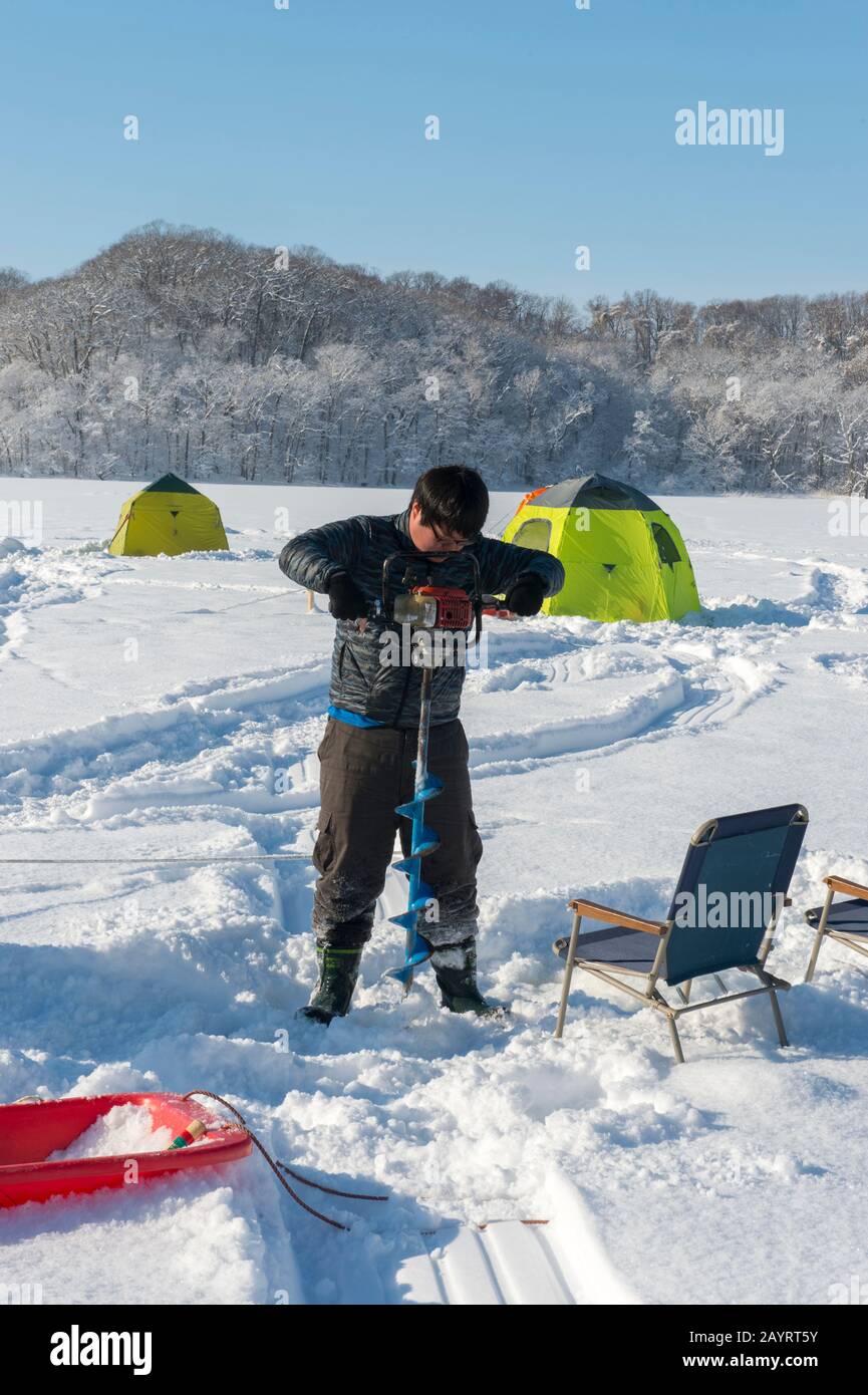 Un homme forge un trou dans la glace pour la pêche sur le lac gelé Abashiriko près d'Abashiri, une ville de l'île Hokkaido, au Japon. Banque D'Images