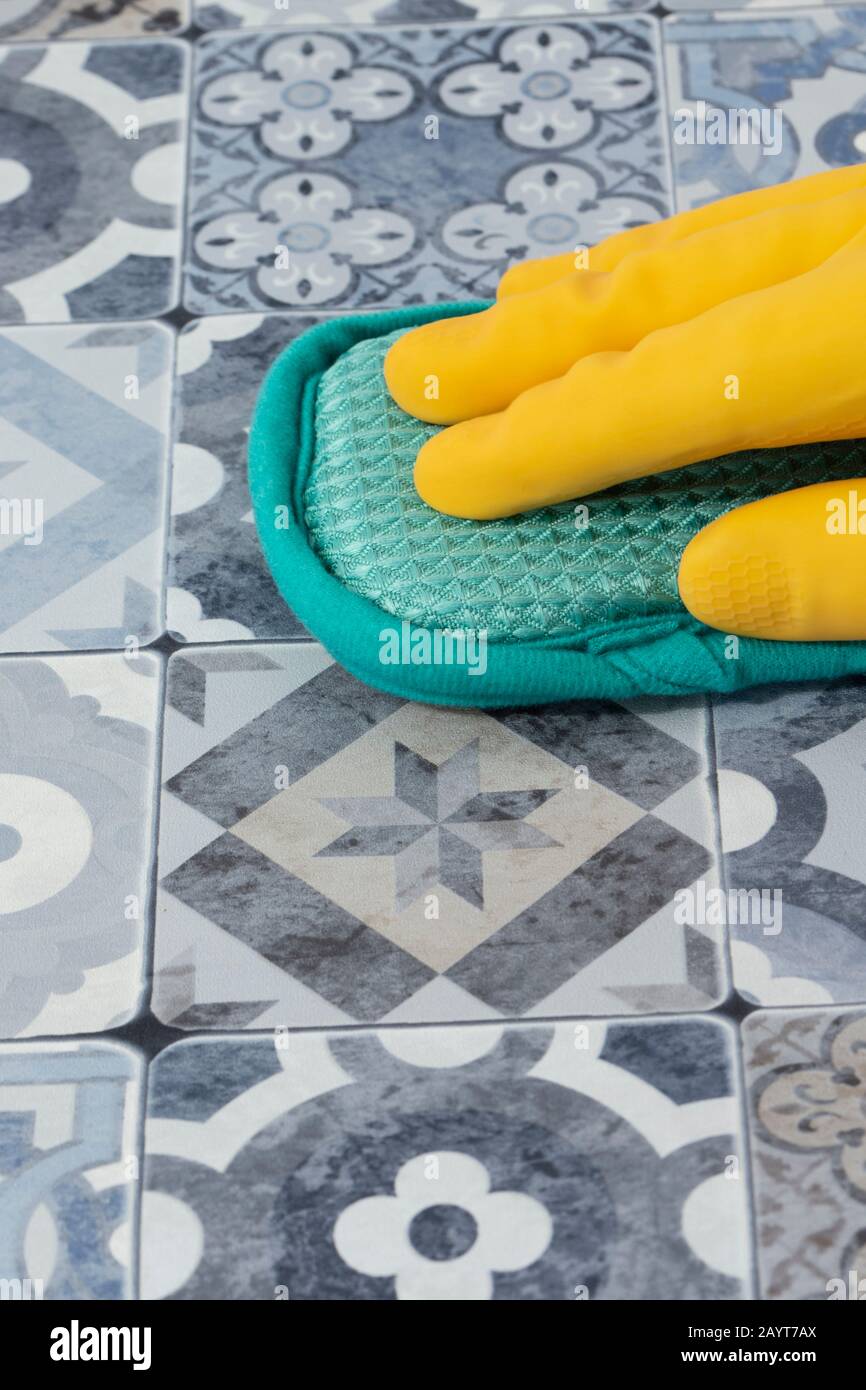 Personne portant des gants en caoutchouc nettoyant des carreaux bleus et blancs sur un plan de travail de cuisine avec une éponge. Banque D'Images