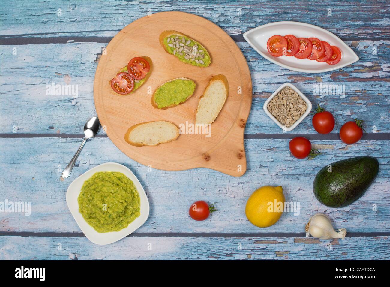 Fabrication de sandwichs à face ouverte. L'avocat se répand avec de l'ail et du jus de citron, des tranches de tomates cerises, des amandes décortiquées de tournesol et des morceaux de pain. Banque D'Images