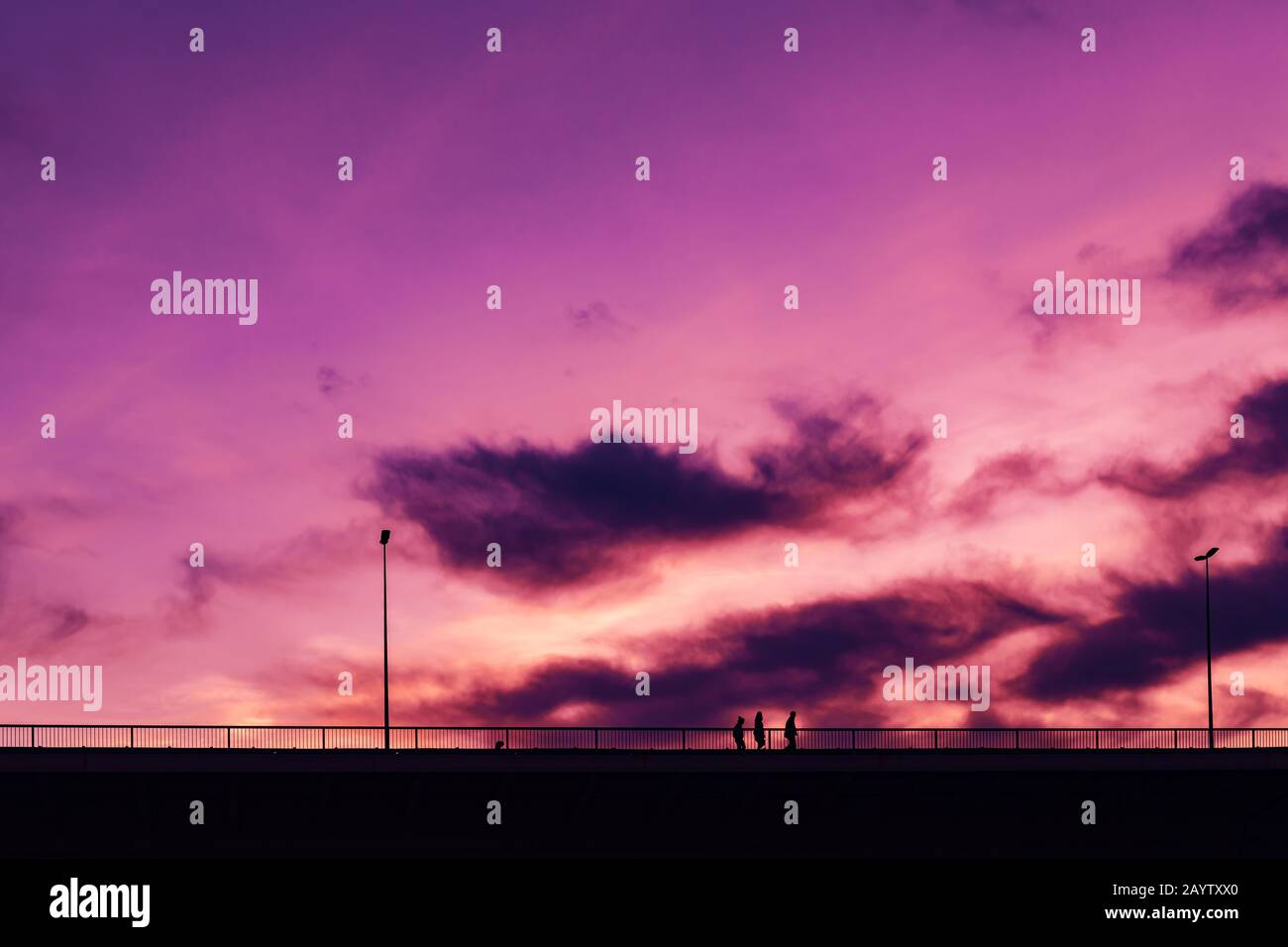 Silhouettes de trois jeunes non reconnaissables traversant le pont au coucher du soleil avec beau ciel violet en arrière-plan Banque D'Images