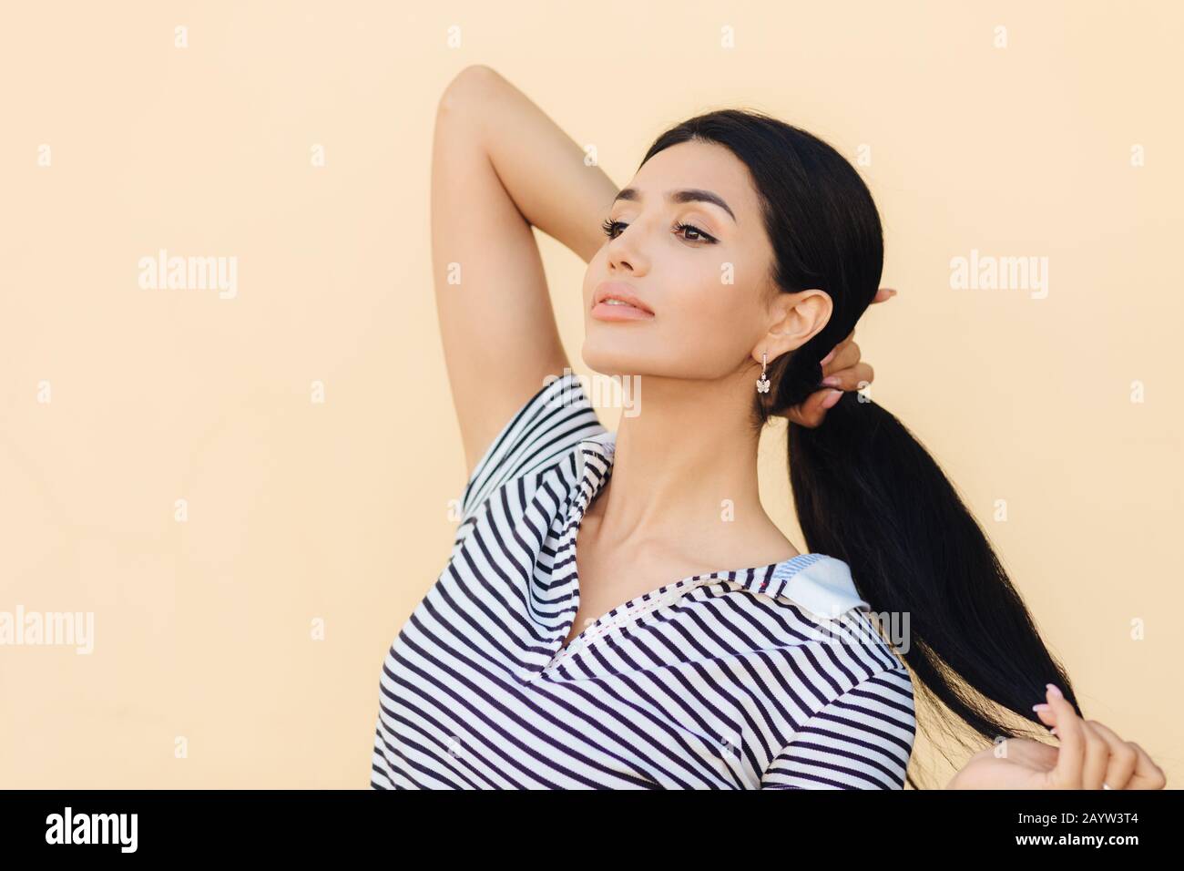 La photo latérale d'une bonne femme brunette garde les cheveux dans la queue de poney, regarde en toute confiance à distance, pense à quelque chose, montre son luxueux hai Banque D'Images