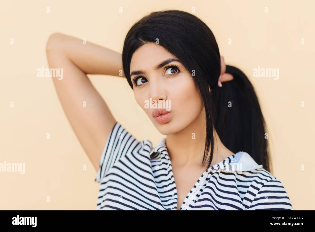 Jolie jeune femme a une expression rêveuse, garde les lèvres rondes, a maquillage, fait des cheveux dans la queue de poney, rêve sur quelque chose, semble pensivement, isolé o Banque D'Images