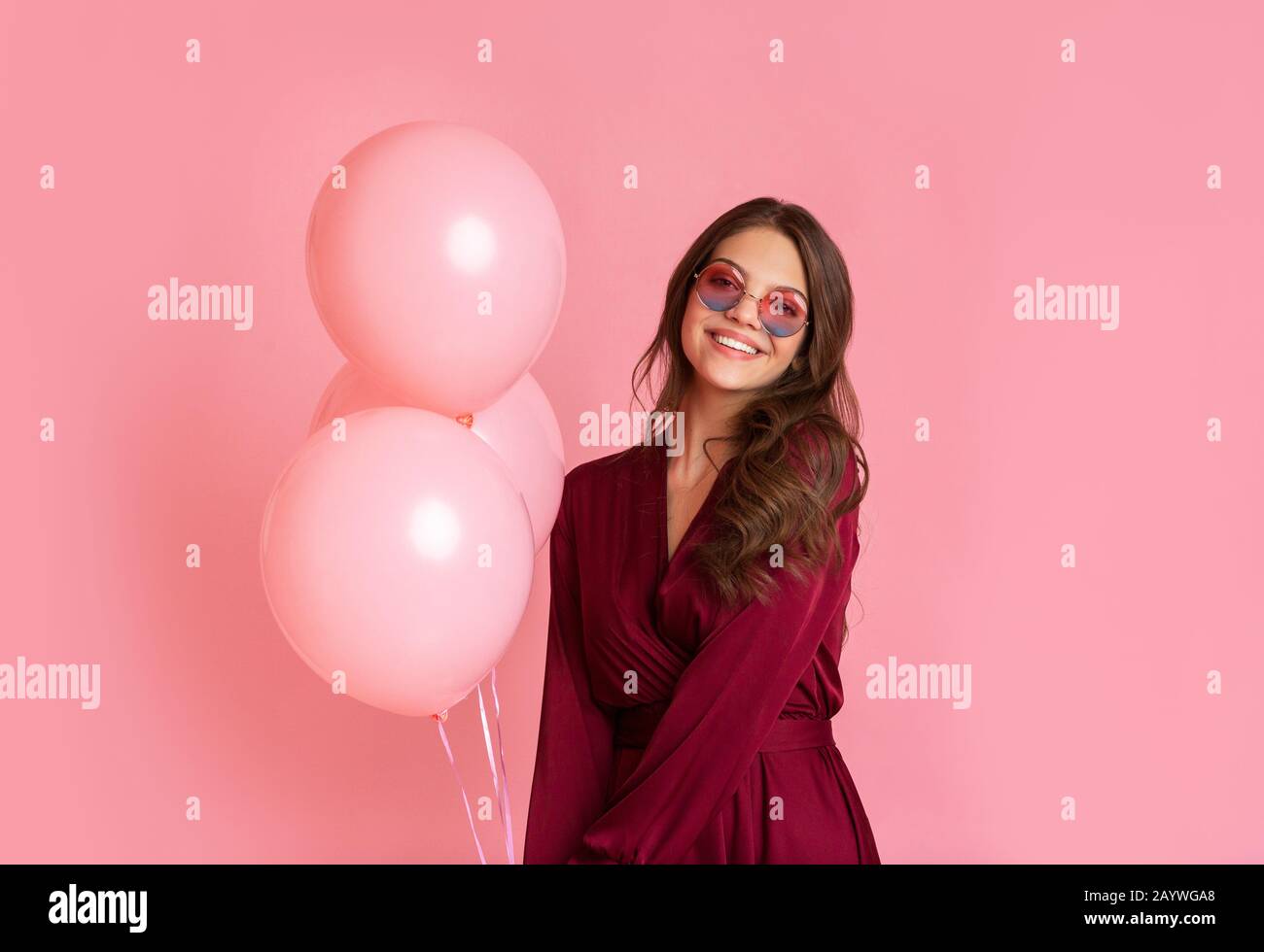 Jolie Fille Dans Des Lunettes De Soleil Stylées Se Posant Avec Des Ballons Sur Fond Rose Banque D'Images