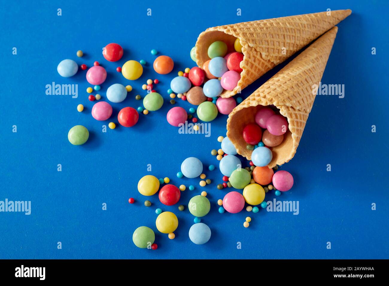 Fond de fête avec des bonbons au chocolat enrobés de sucre colorés dispersés sur des cônes bleus et de glace de gaufre dans une couche plate encore la vie avec espace de copie Banque D'Images