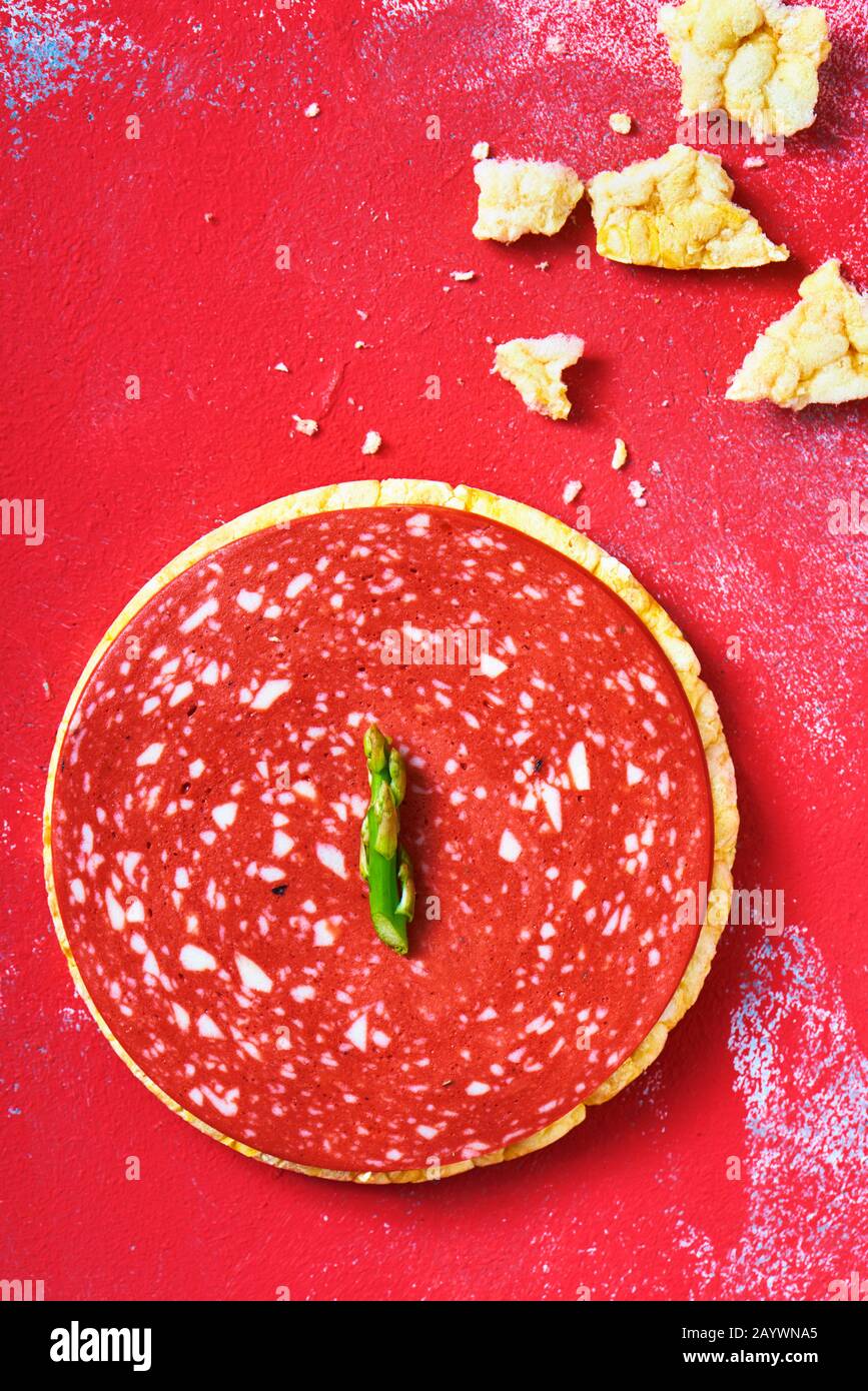 vue en grand angle d'une tranche de salami végétalien sur un gâteau de riz, sur une surface rouge texturée Banque D'Images