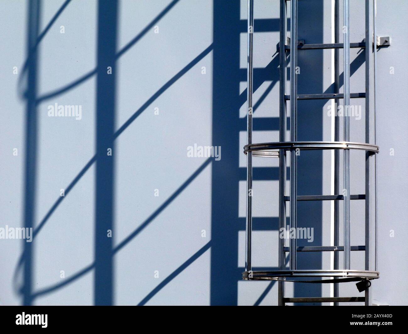 vue abstraite détaillée de l'échelle d'accès au toit en aluminium. cage de sécurité. boulonnée au mur en béton. longues ombres au soleil brillant l'après-midi. industrie de la construction. Banque D'Images