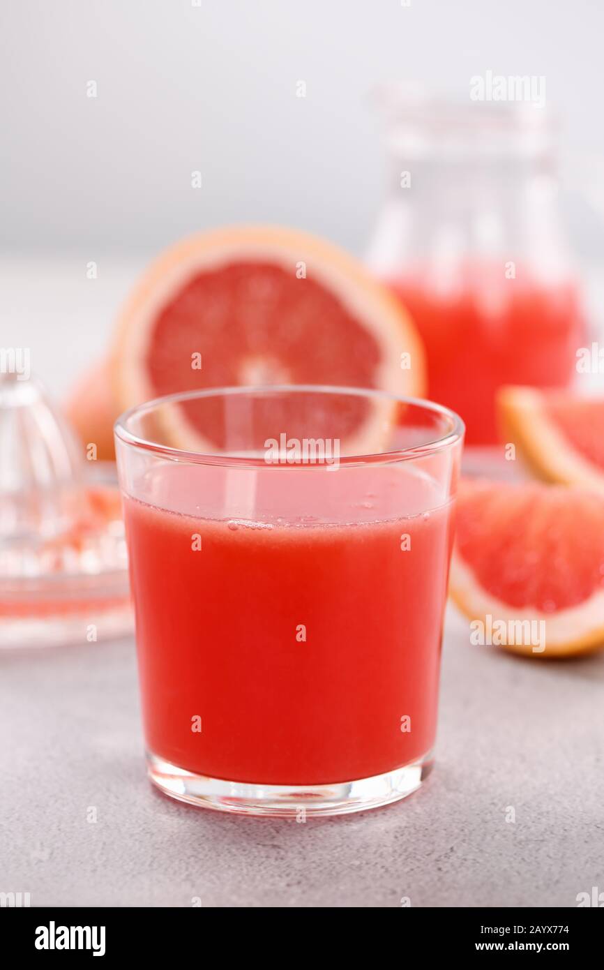 Un verre de jus de pamplemousse fraîchement préparé et des tranches de fruits frais sur un fond en béton léger. Boisson saine et alimentation. Gros plan Banque D'Images