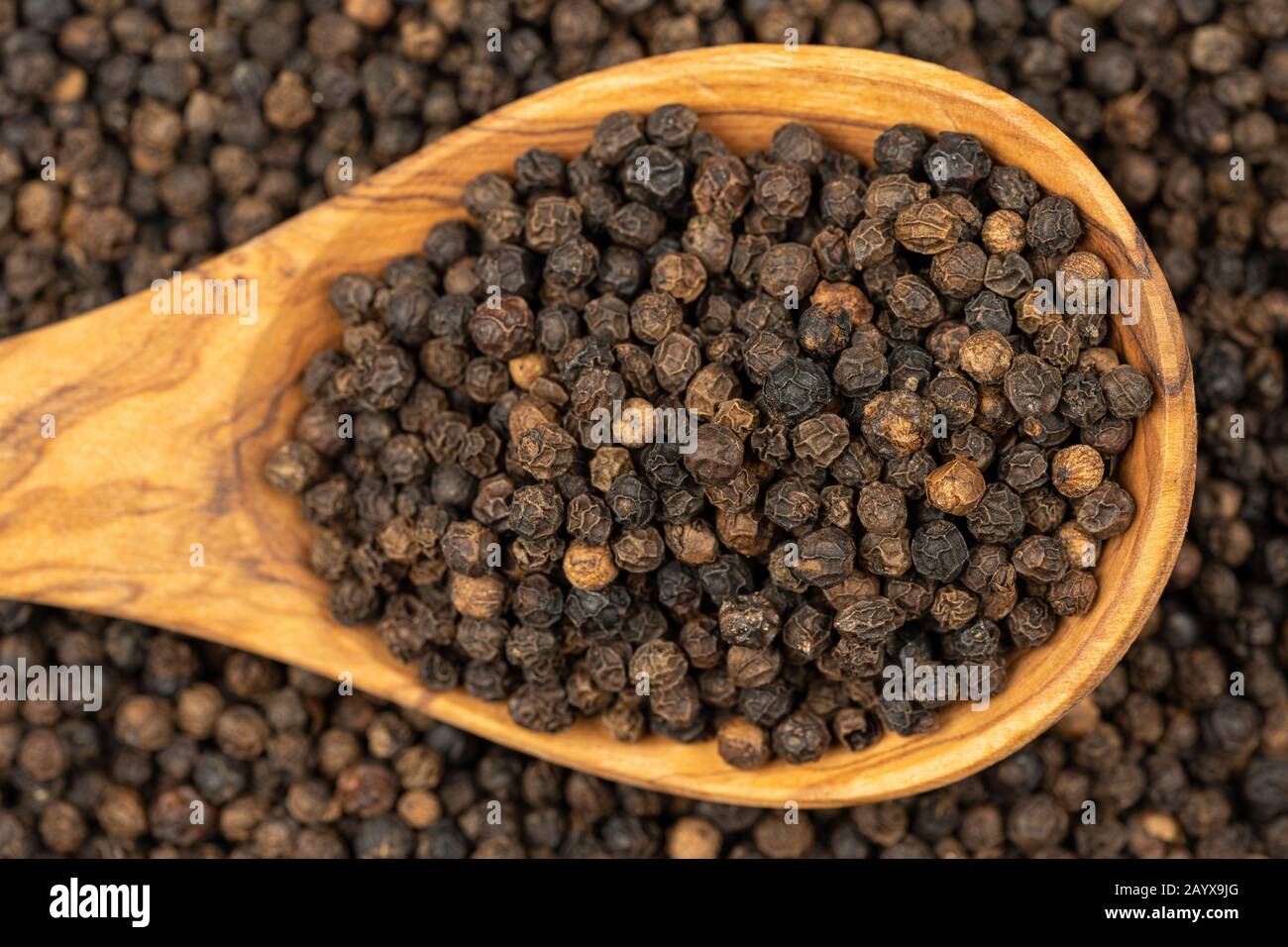 Fond d'épices, fond fait de beaucoup de grains entiers de poivre noir et une cuillère de cuisson faite de bois d'olive également rempli de poivre , très proche Banque D'Images