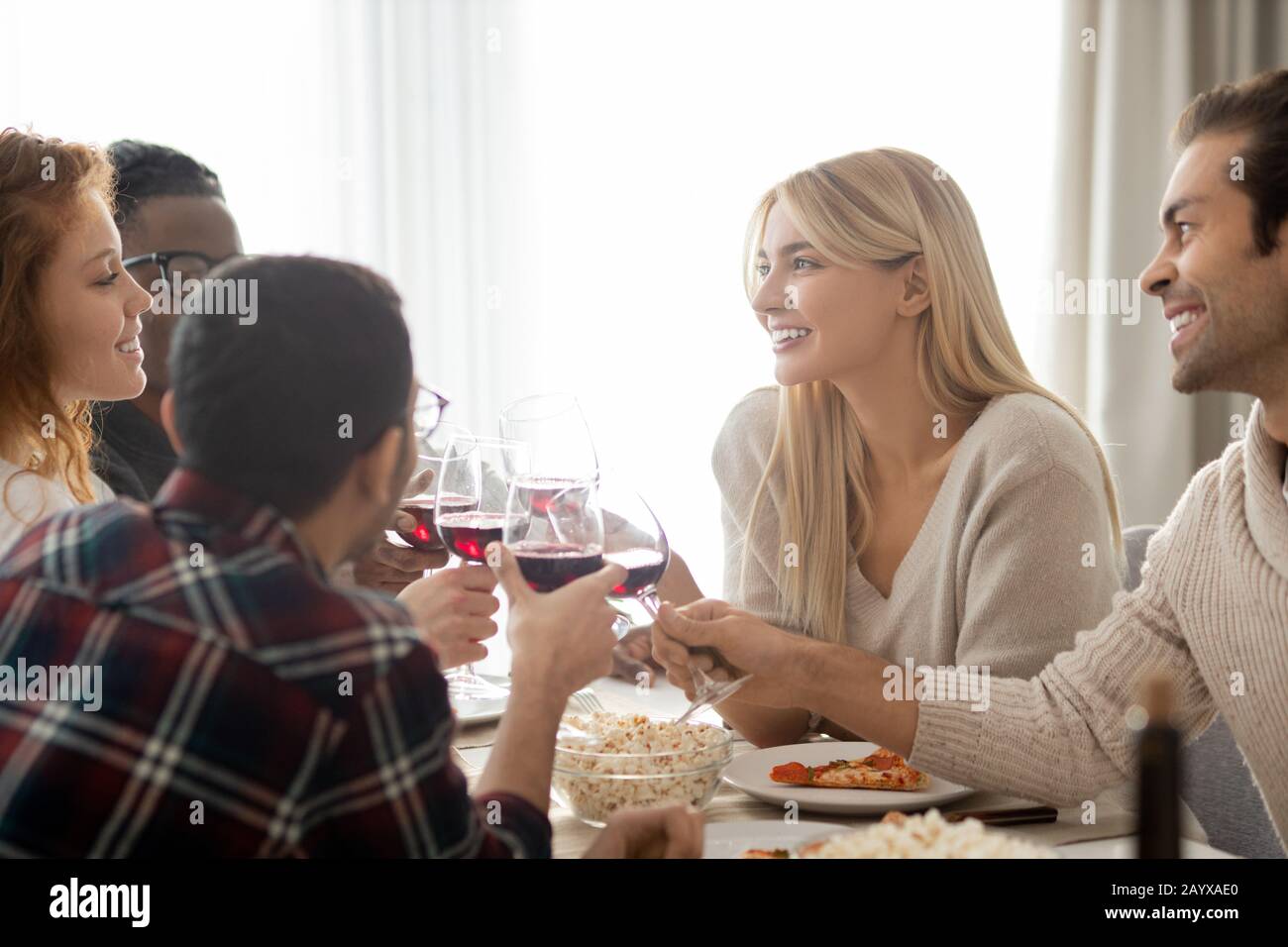 Groupe de jeunes amis multiethniques positifs assis à la table et à la clinking Winelunettes au dîner-fête Banque D'Images