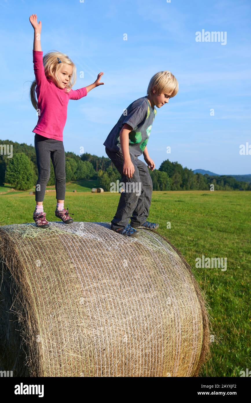 Un jeune enfant garçon et fille (frères et sœurs) jouant sur la balle de foin l'été. Activités de plein air pour les enfants en été. Sautez de haut en haut. Concept d'été Banque D'Images