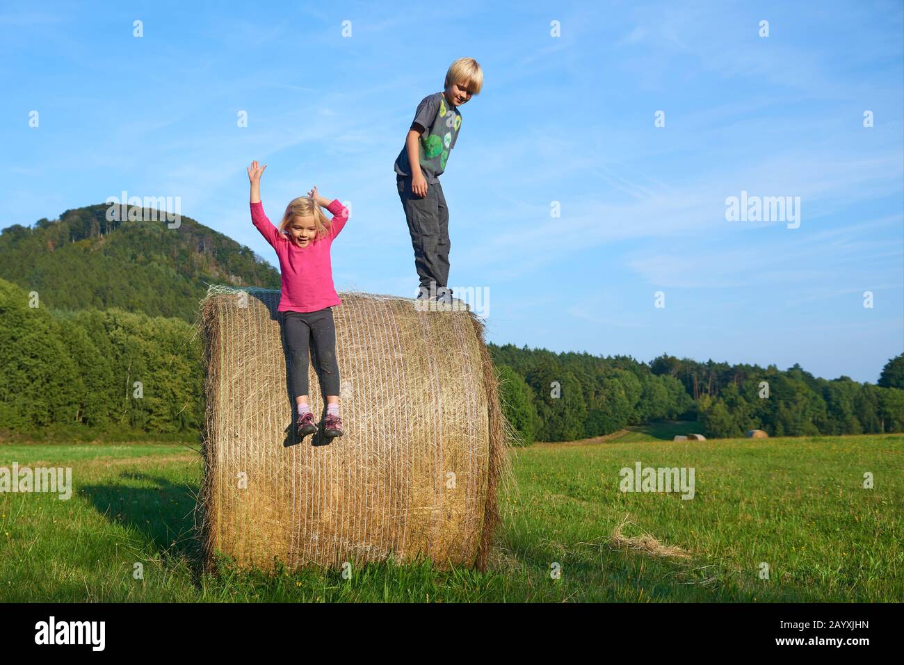 Un jeune enfant garçon et fille (frères et sœurs) jouant sur la balle de foin l'été. Activités de plein air pour les enfants en été. Sautez de haut en haut. Concept d'été Banque D'Images
