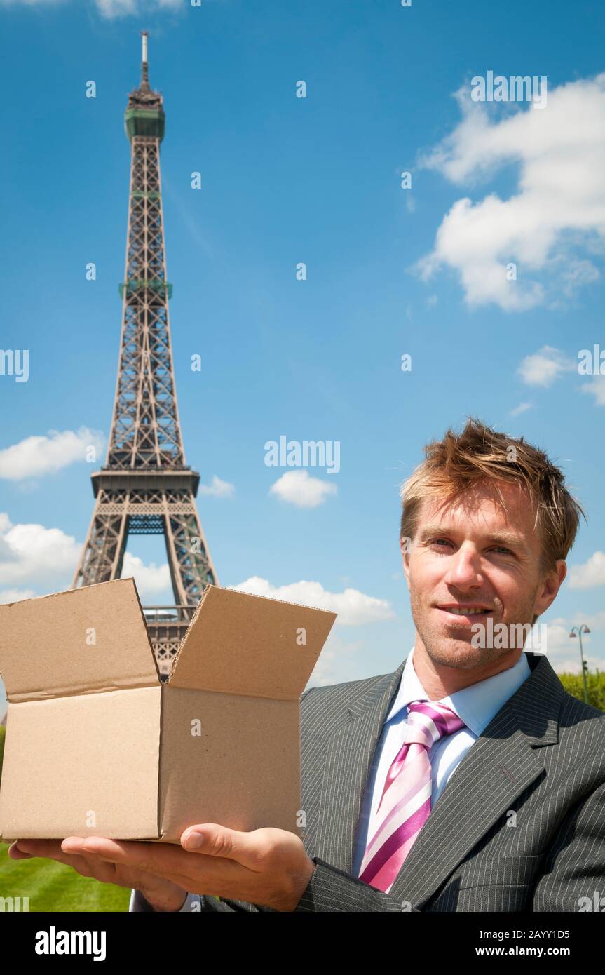 Un homme d'affaires européen souriant qui tient une boîte en carton marron avec la Tour Eiffel en train de se retirer lors d'une journée d'été à Paris, en France Banque D'Images