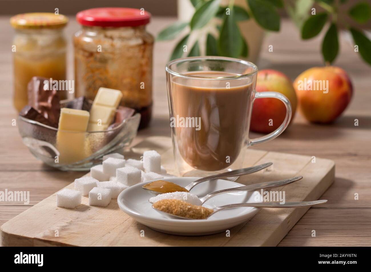 Le sucre en morceaux, le sucre de canne, le sucre blanc en vrac et le miel de sarrasin sur une cuillère à café se trouve à côté d'un verre avec du café et du lait. En arrière-plan chocolat et Banque D'Images