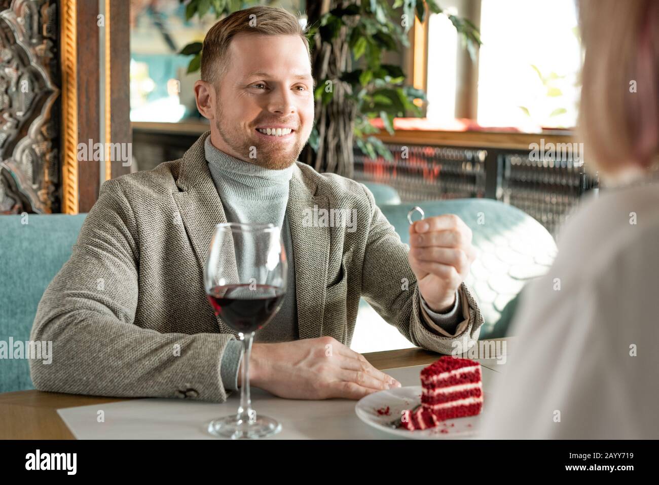 Photo horizontale sur l'épaule d'un jeune homme heureux proposant à une femme non reconnaissable assise devant lui dans un restaurant moderne Banque D'Images