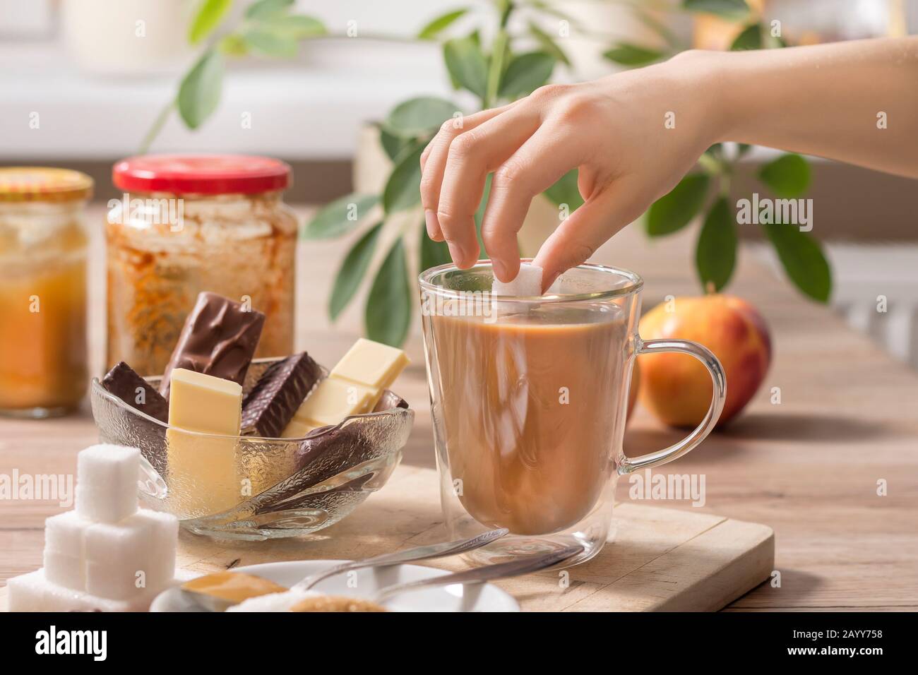 La main du garçon tient un cube de sucre sur un verre de thé ou de café avec du lait. Différents types de bonbons et de sucre se trouvent sur la table. Banque D'Images