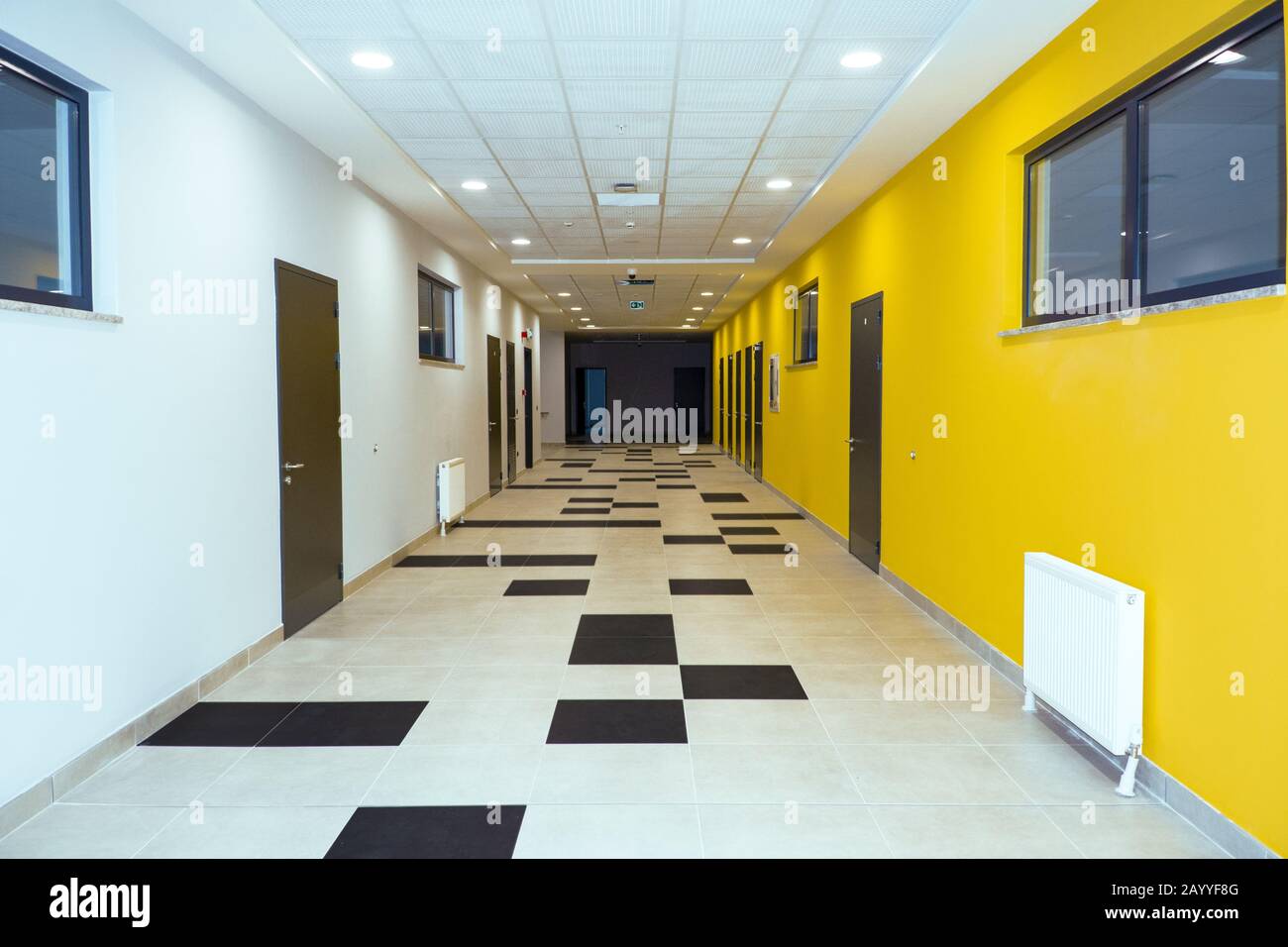 Couloir scolaire avec murs jaune et blanc, meublé de tuiles noires et blanches Banque D'Images