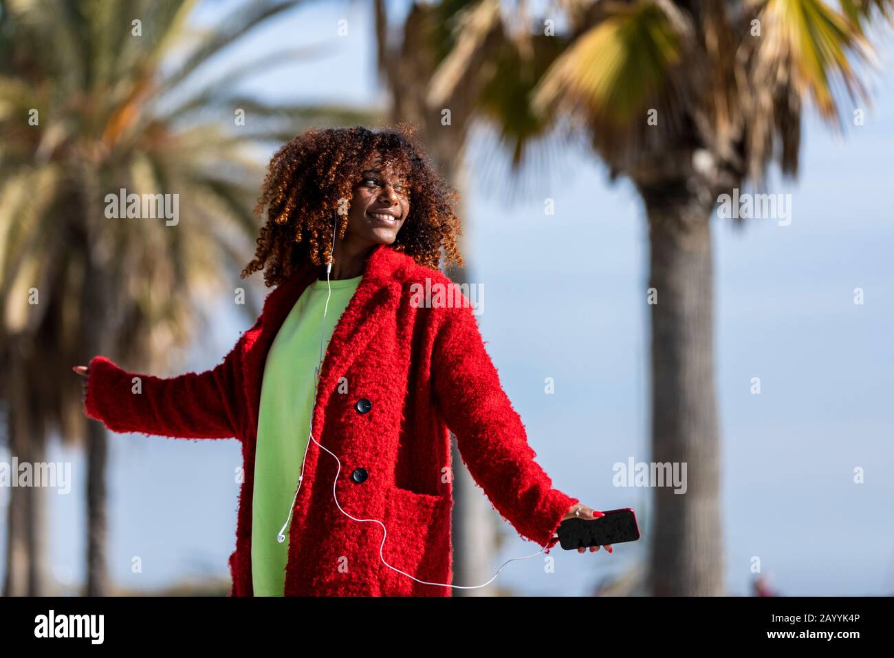 Jeune afro american femme riant tout en dansant dehors avec une veste rouge Banque D'Images