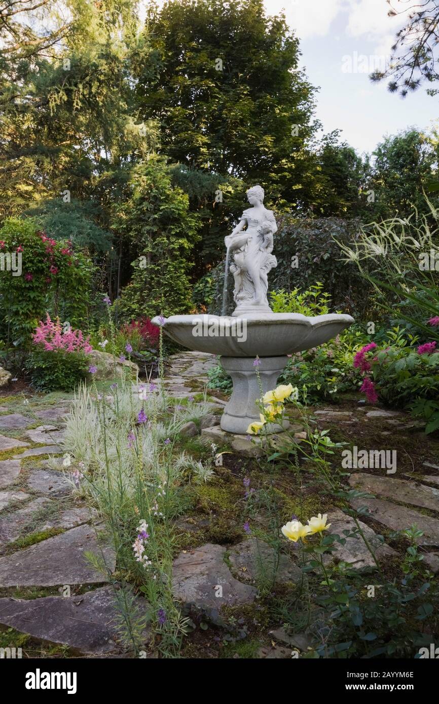 Sentier en pierre de flagelle, fontaine d'eau et frontières avec plantes ornementales, jaune Rosa «Flower Carpet» - Roses, philippin purpurea «Elegans». Banque D'Images