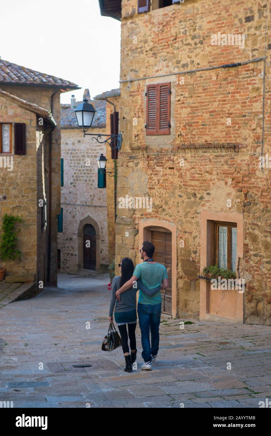 Scène de rue avec couple marchant dans la ville médiévale de Montichiello dans le Val d'Orcia près de Pienza en Toscane, Italie. Banque D'Images