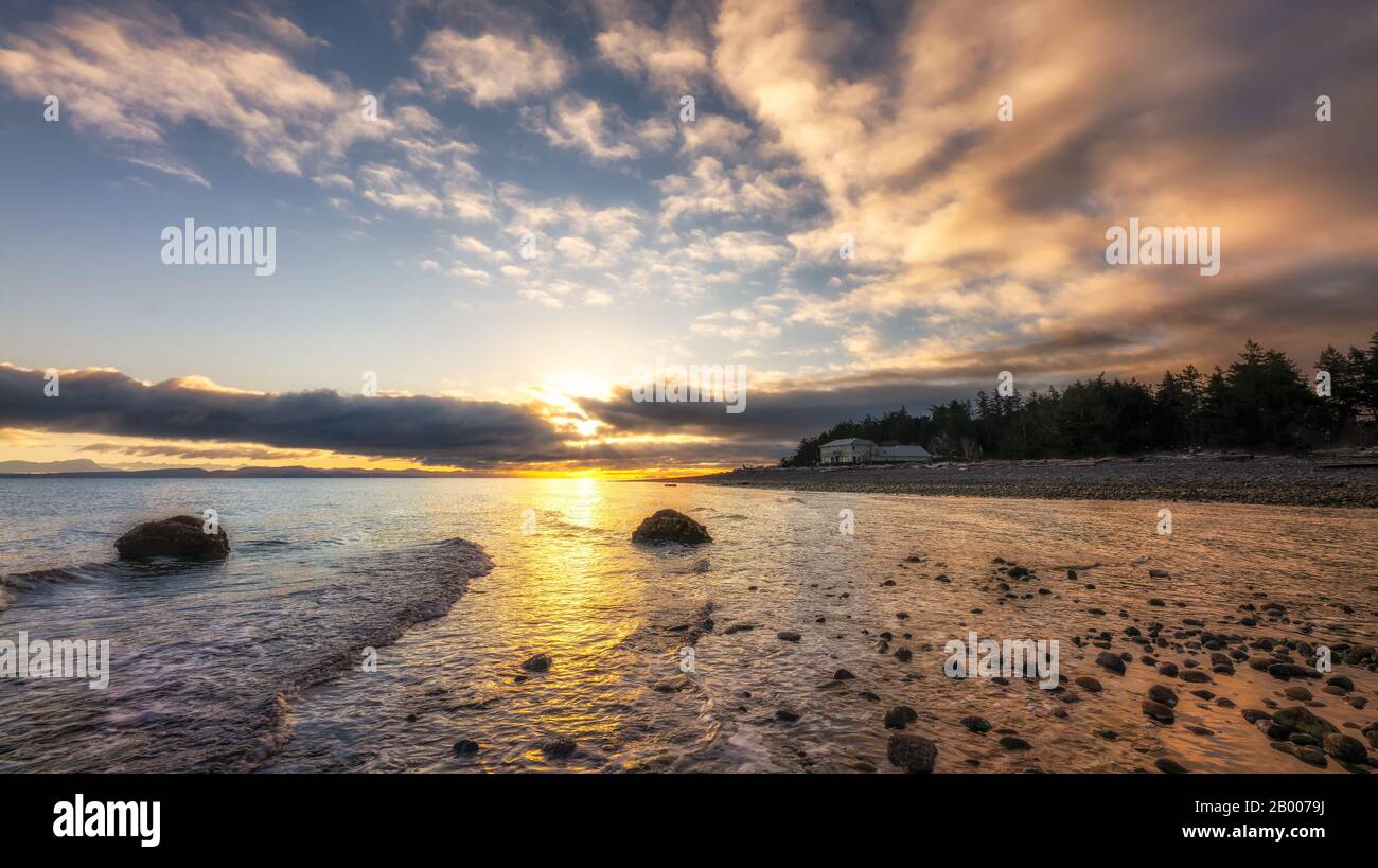 Magnifique lever de soleil sous des nuages spectaculaires le long d'une rive avec une maison isolée. Banque D'Images