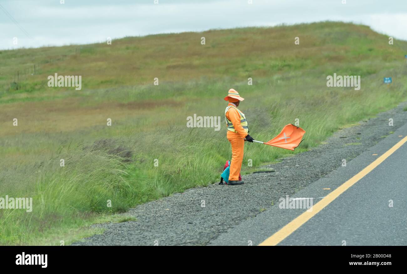 Ouvrier africain agitant un drapeau et vêtu de vêtements de haute visibilité ou uniforme et faisant partie d'une équipe de travaux routiers en Afrique du Sud Banque D'Images