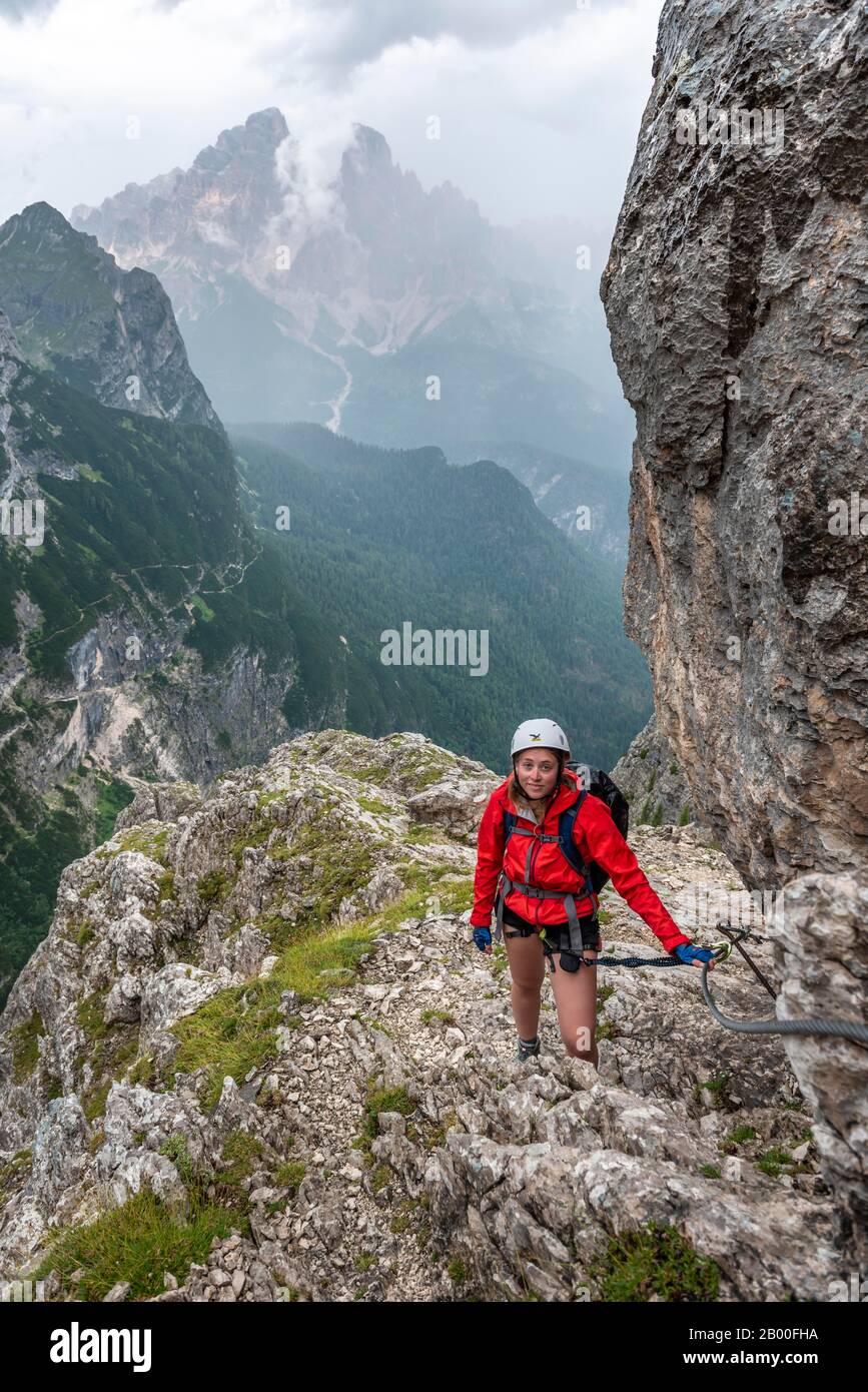 Jeune femme, randonneur grimpant sur la via ferrata Vandelli, circuit de Sorapiss, montagnes à faible nuage, Dolomites, Belluno, Italie Banque D'Images