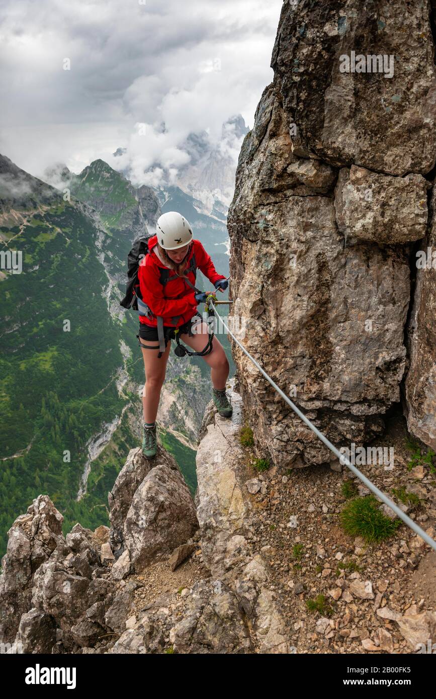 Jeune femme, randonneur grimpant sur un rocher dans une via ferrata Vandelli, circuit de Sorapiss, montagnes à faible nuage, Dolomites, Belluno, Italie Banque D'Images