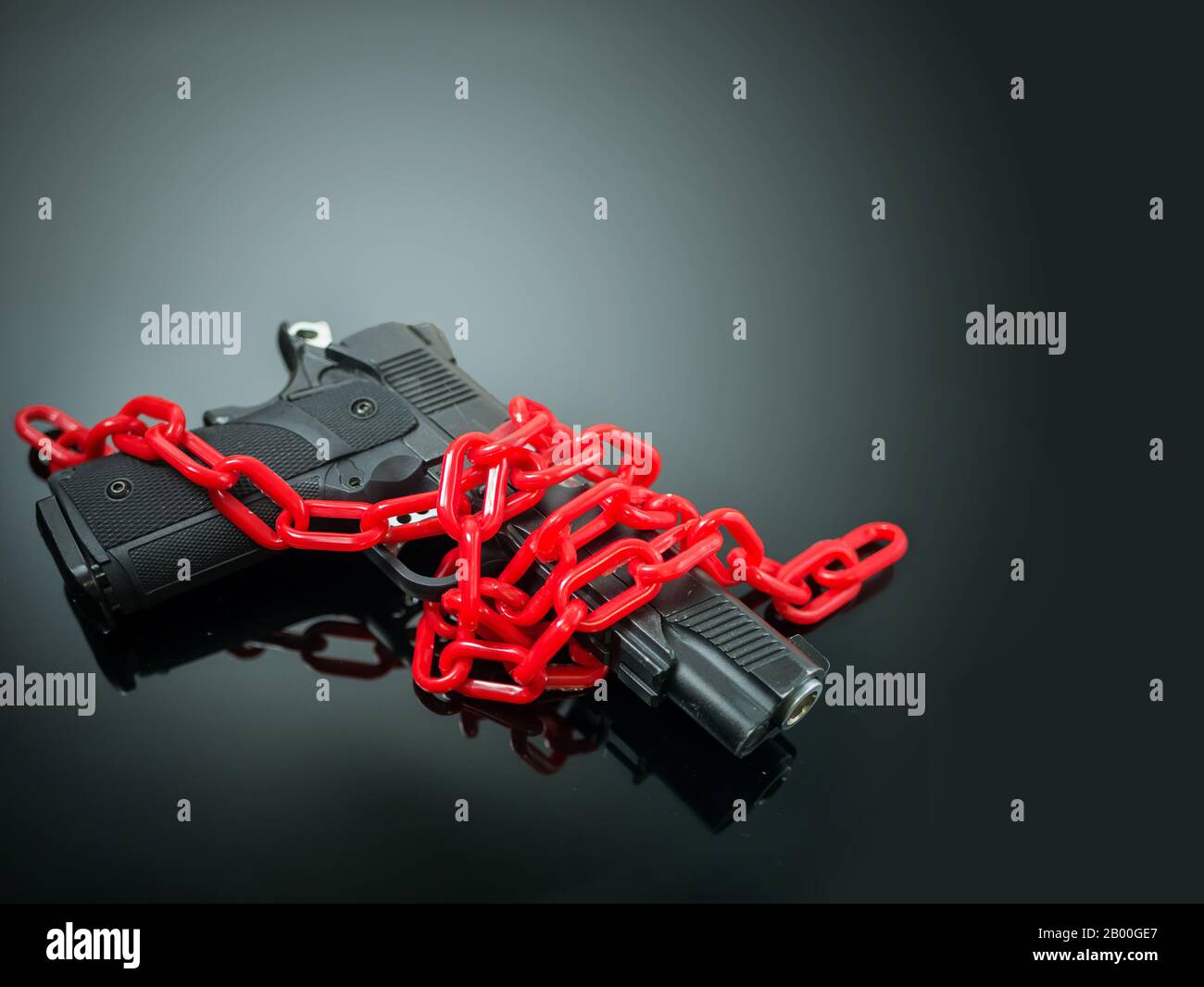 réformer le concept de contrôle des armes à feu. la chaîne rouge autour du pistolet sur le miroir noir avec le projecteur briller sur le pistolet Banque D'Images