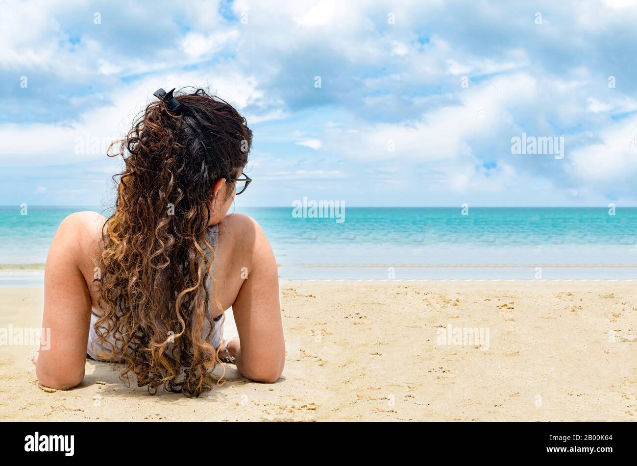 Vue sur le dos pose de jeune fille attrayante et belle au début des années 20 avec des poils longs et colorés, tout en se bronzant à la plage le jour ensoleillé. Banque D'Images