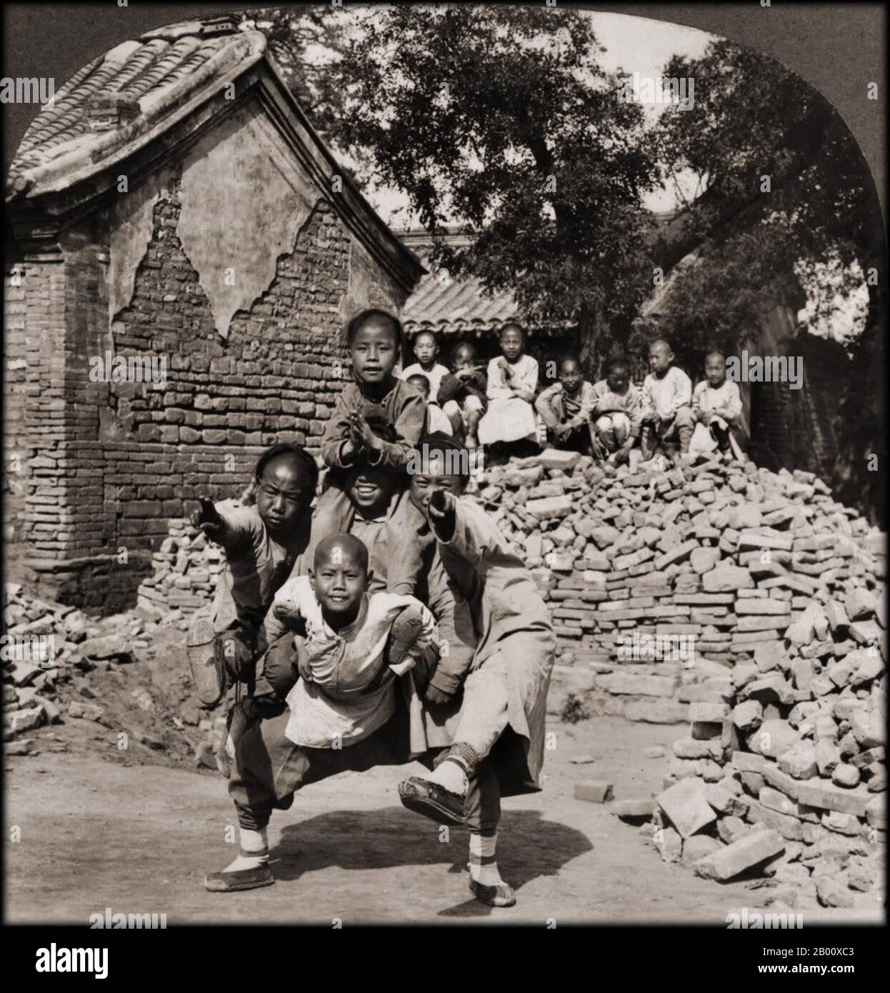 Chine: Cinq enfants jouent formant une posture de 'tête de'', 1902. La dynastie Qing (1644–1911) a été fondée après que les Manchus ont vaincu le Ming, la dernière dynastie chinoise Han. Les Manchus ont introduit un « ordre de file d'attente », obligeant les Chinois Han à adopter la coiffure de file d'attente de Manchu et des vêtements de style Manchu. Le Qing a consolidé le contrôle de certaines zones initialement sous le Ming, y compris le Yunnan. Ils ont également étendu leur sphère d'influence au Xinjiang, au Tibet et à la Mongolie. Mais au cours du XIXe siècle, le contrôle de Qing s'est affaibli, avec son effondrement final au début du XXe siècle. Banque D'Images