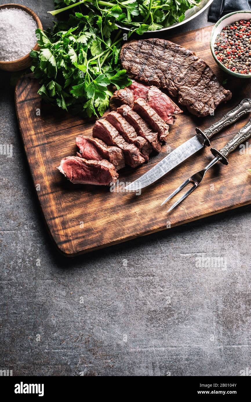 Tranches de steak de bœuf grillé juteux avec fourchette et couteau sur une  plaque de boucher Photo Stock - Alamy