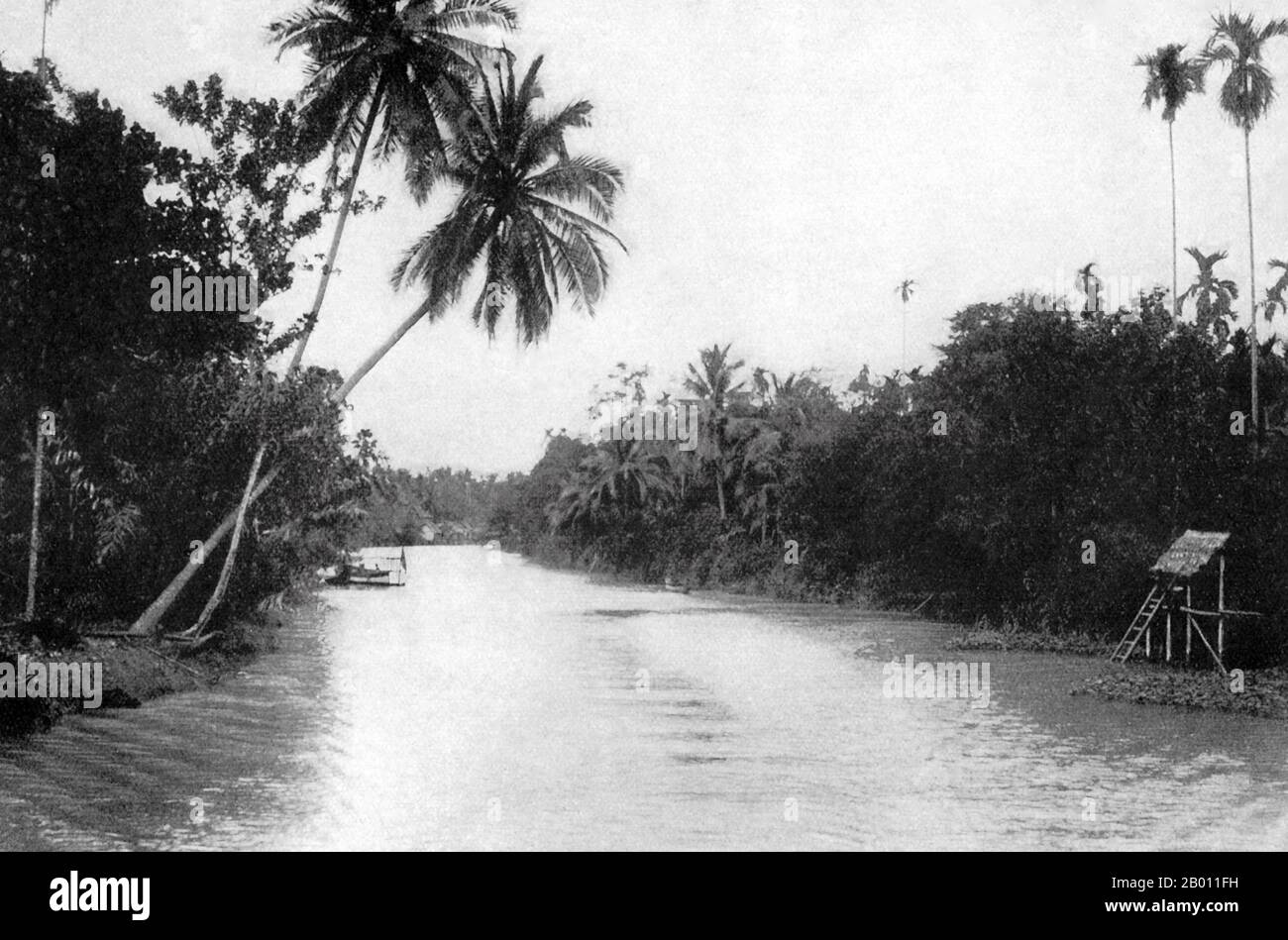 Thaïlande: Une scène de canal de l'extérieur de Bangkok, c. 1900. Au tournant du XXe siècle, la grande majorité des Siamois étaient des riziculteurs qui vivaient et travaillaient le long des cours d'eau. Chaque ménage avait un bateau, dont environ 600,000 navigué sur les canaux et les rivières de Bangkok. L'aviron a été fait de l'arrière du bateau. La plupart des maisons étaient en bois et en bambou, et ont été construites sur pilotis avec une échelle allant à l'eau. Sur la rive droite de la rivière se trouvent de grands palmiers arecas droits qui fournissent des noix de bétel; sur la gauche, des cocotiers. Banque D'Images