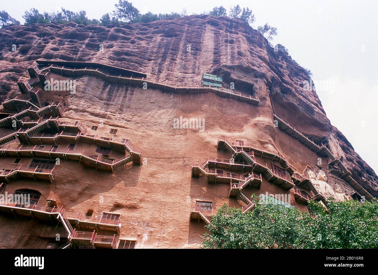 Chine : des escaliers sillonnent les grottes de Maiji Shan, Tianshui, province de Gansu.Maijishan Shiku (grottes de Maiji Shan) est l’un des quatre groupes de temples bouddhistes les plus importants de Chine (les autres étant Datong, Luoyang et les grottes de Mogao à Dunhuang).À partir des dynasties de Wei du Nord (386-535) et de Zhou du Nord (557-81), les bouddhistes tachent des grottes sur les côtés d'un affleurement rouge qui s'élève des collines couvertes de feuillage environnantes.Les figures du Bouddha, des bodhisattvas et des disciples ont été sculptées dans le rocher plus dur apporté d'ailleurs, et installées dans les grottes. Banque D'Images