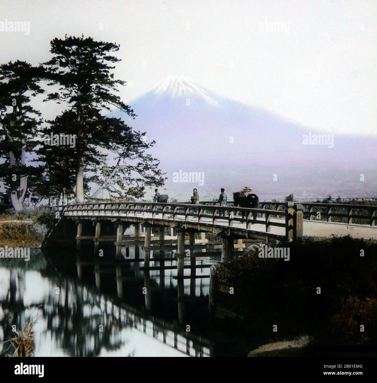 Japon : traversée d'un pont sous le Mont Fuji, Enami Nobukuni (1859-1929), vers 1910. T. Enami (Enami Nobukuni) était le nom commercial d'un célèbre photographe de l'époque Meiji. Le T. de son nom commercial est censé avoir représenté Toshi, bien qu'il ne l'ait jamais écrit sur aucun document personnel ou d'affaires. Né à Edo (aujourd'hui Tokyo) pendant l'ère Bakumatsu, Enami a d'abord été étudiant, puis assistant du célèbre photographe et collectionniste, Ogawa Kazumasa. Enami a déménagé à Yokohama, et a ouvert un studio sur Benten-dōri (rue Benten) en 1892. Banque D'Images