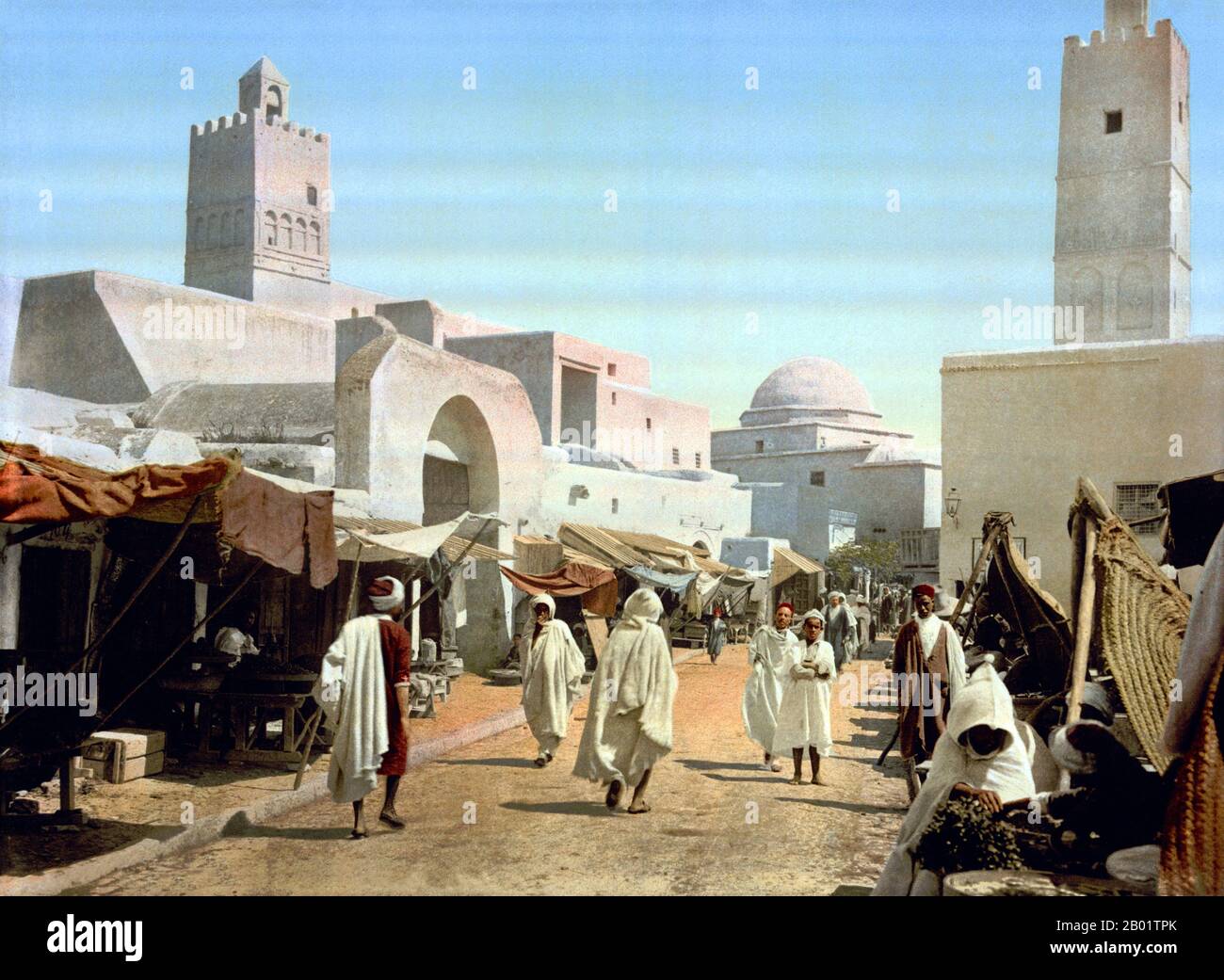 Tunisie : rue principale et mosquée à Qairawan/Kairouan, 1899. Kairouan (Al Qairawān), également connu sous le nom de Kirwan ou al-Qayrawan, est la capitale du gouvernorat de Kairouan en Tunisie. Appelée capitale culturelle islamique, elle est classée au patrimoine mondial de l'UNESCO. La ville a été fondée par les Arabes vers 670. À l'époque du calife Mu'awiya (R. 661-680), il est devenu un centre important pour l'apprentissage islamique et coranique, attirant ainsi un grand nombre de musulmans de diverses parties du monde, à côté seulement de la Mecque et Médine. La sainte mosquée d'Uqba est située dans la ville. Banque D'Images