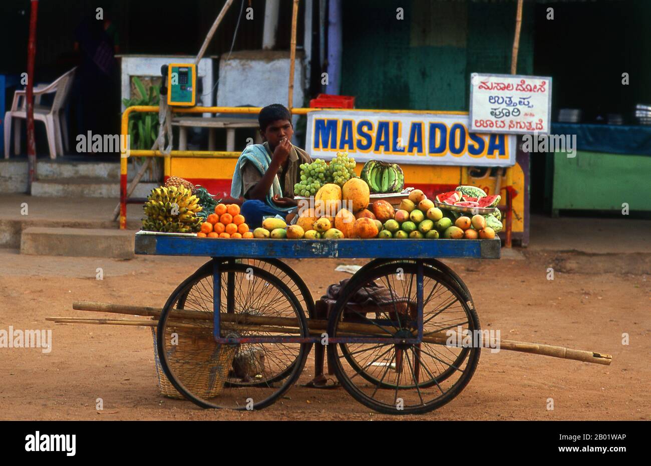 Inde : vendeur de fruits dans l'ancien Hampi, État du Karnataka. Hampi est un village du nord de l'État du Karnataka. Il est situé dans les ruines de Vijayanagara, l'ancienne capitale de l'Empire Vijayanagara. Antérieure à la ville de Vijayanagara, elle continue d'être un important centre religieux, abritant le temple Virupaksha, ainsi que plusieurs autres monuments appartenant à la vieille ville. Banque D'Images