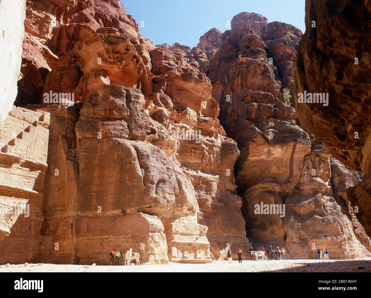 Jordanie : visiteurs entrant dans la rue des façades, Petra. Pétra a été établie pour la première fois comme une ville par les Arabes nabatéens au IVe siècle av. J.-C., et doit sa naissance et sa prospérité au fait qu'elle était le seul endroit avec une eau claire et abondante entre les centres commerciaux du Hijaz de la Mecque et Médine, et la Palestine. Creusée directement dans les crêtes de grès nubiennes du désert du sud de la Jordanie, il semble probable que - compte tenu de son excellente position défensive et de ses bonnes réserves d'eau - Petra a été continuellement occupée dès l'époque paléolithique. On pense qu'il est mentionné dans la Bible. Banque D'Images