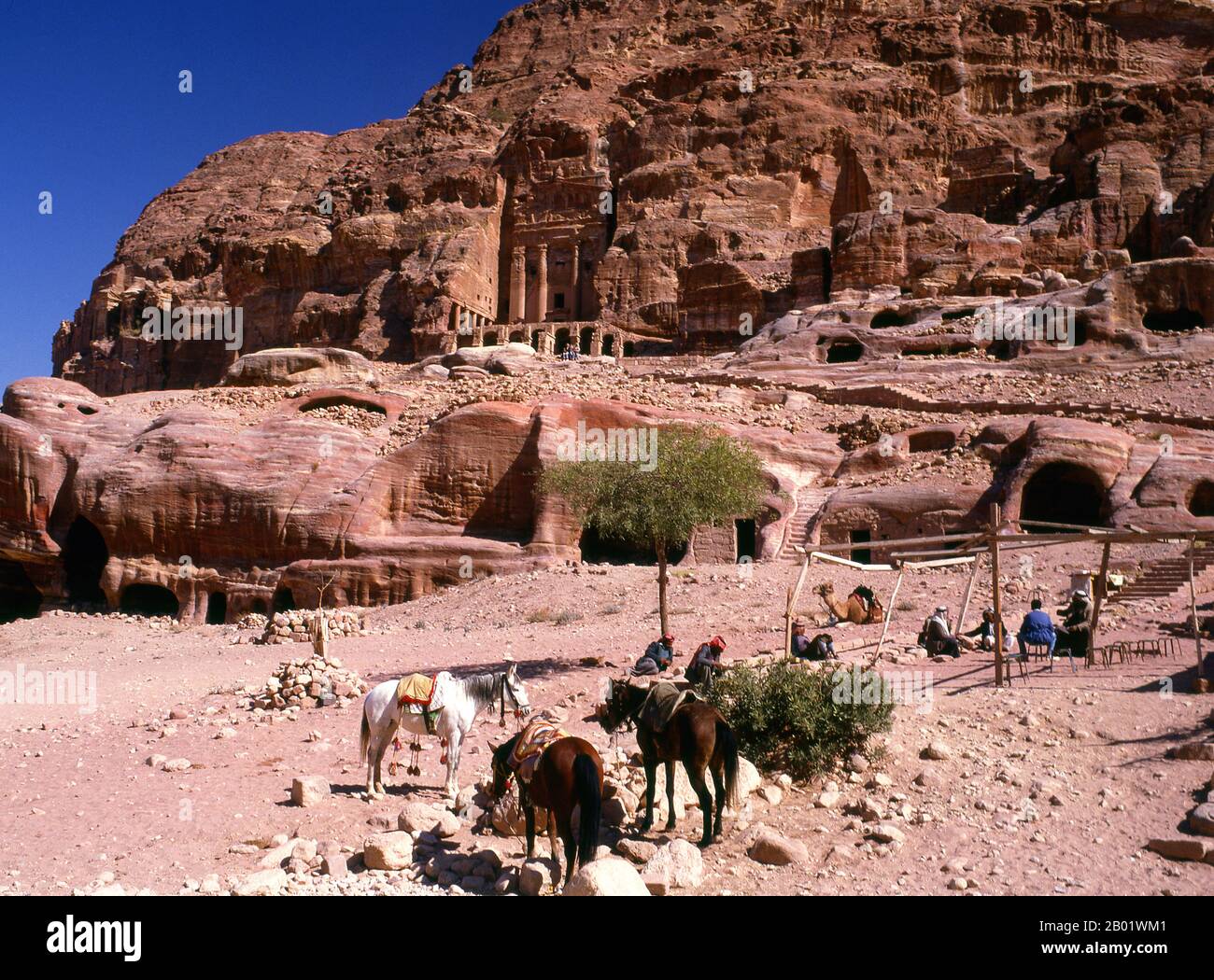 Jordanie : cavaliers arabes devant le tombeau de l'urne, Petra. Pétra a été établie pour la première fois comme une ville par les Arabes nabatéens au IVe siècle av. J.-C., et doit sa naissance et sa prospérité au fait qu'elle était le seul endroit avec une eau claire et abondante entre les centres commerciaux du Hijaz de la Mecque et Médine, et la Palestine. Creusée directement dans les crêtes de grès nubiennes du désert du sud de la Jordanie, il semble probable que - compte tenu de son excellente position défensive et de ses bonnes réserves d'eau - Petra a été continuellement occupée dès l'époque paléolithique. On pense qu'il est mentionné dans la Bible. Banque D'Images