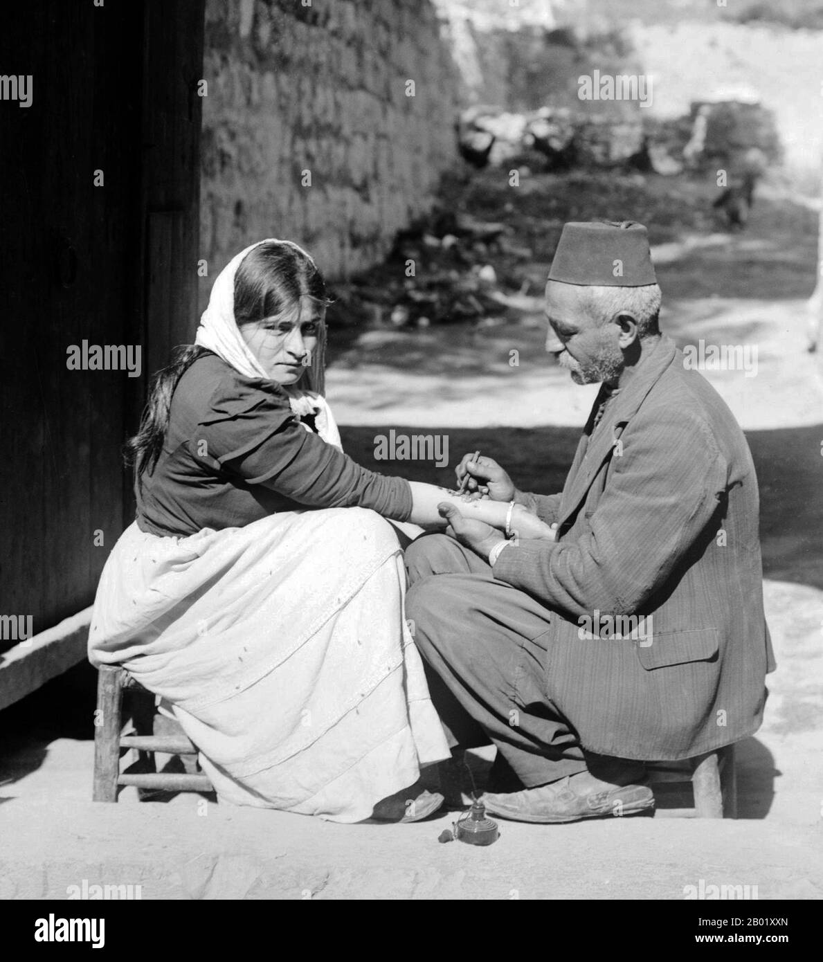 Palestine : homme palestinien tatouant un charme religieux sur l'avant-bras d'une femme chrétienne, v. 1920. Palestine est un nom donné à la région géographique entre la mer Méditerranée et le Jourdain. La région est également connue comme la Terre d'Israël, la Terre Sainte et le Levant Sud. En 1832, la Palestine a été conquise par l'Égypte de Muhammad Ali, mais en 1840, la Grande-Bretagne est intervenue et a rendu le contrôle du Levant aux Ottomans en échange de nouvelles capitulations. La fin du XIXe siècle voit le début de l'immigration sioniste et la renaissance de la langue hébraïque. Banque D'Images